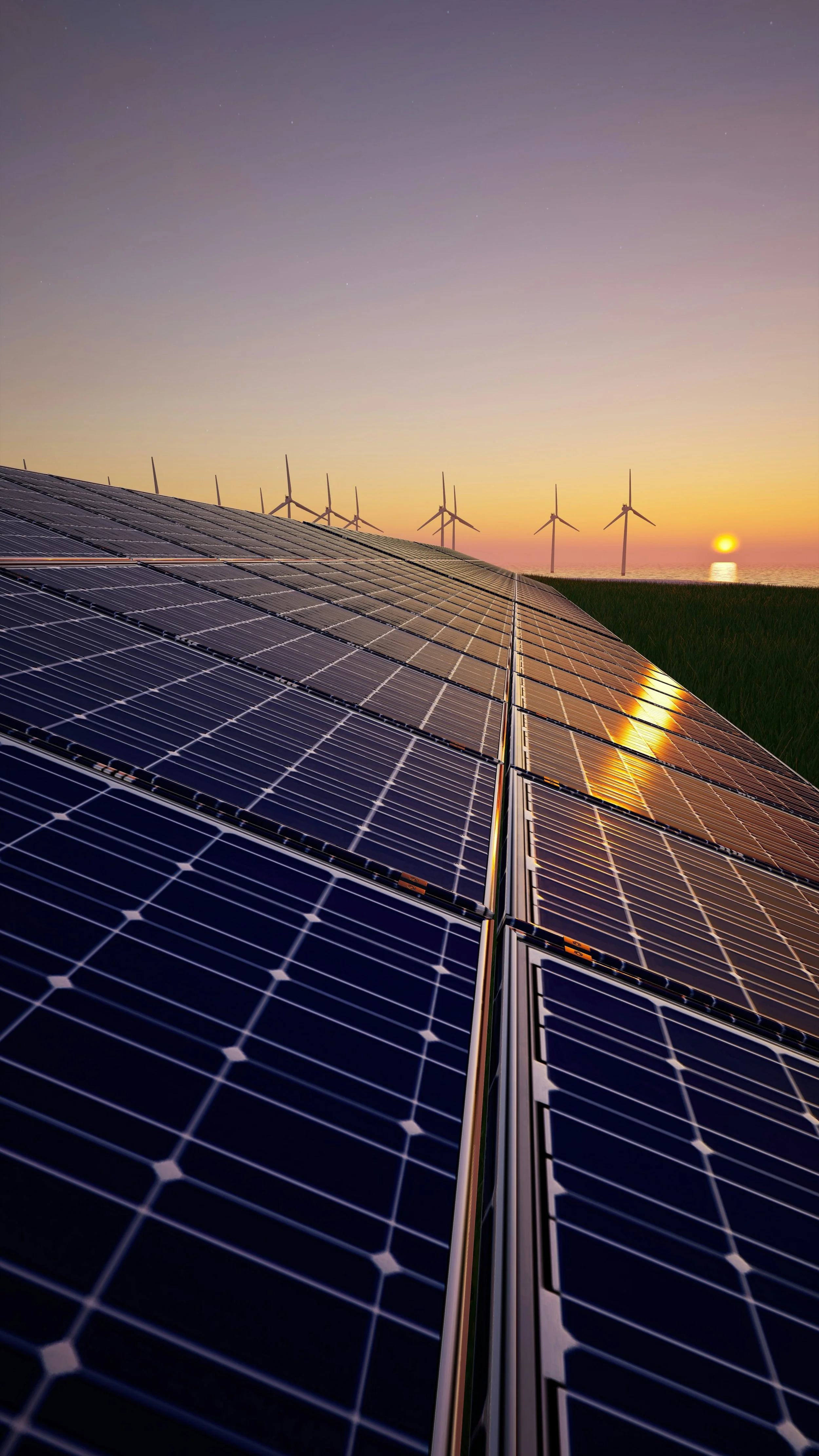 Close-up view of solar panels on a roof at sunset with wind turbines and a setting sun in the background.