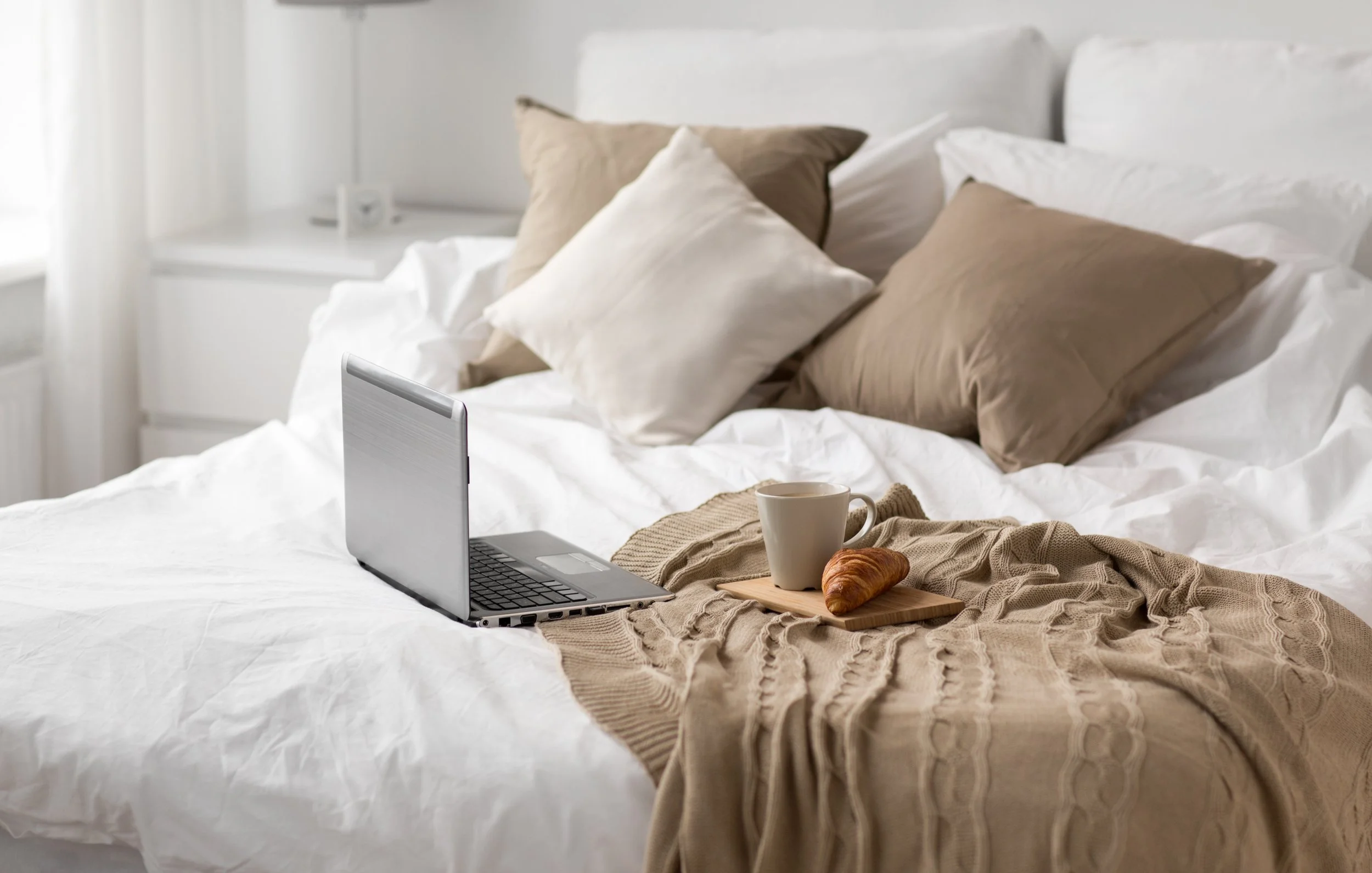 Coffee, bagel, and laptop sitting on a bed