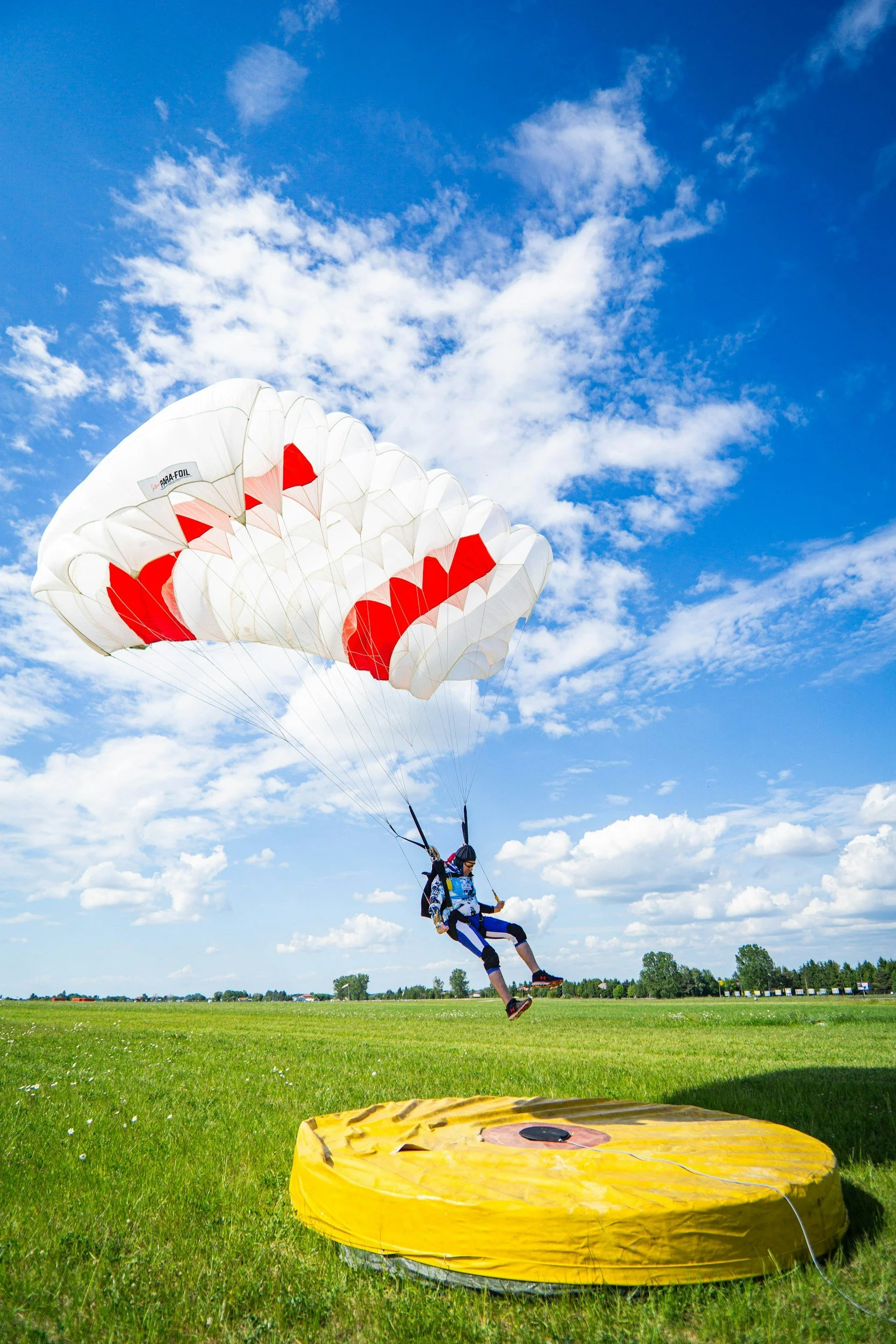 A person paragliding over a grassy field on a sunny day with blue sky and clouds.