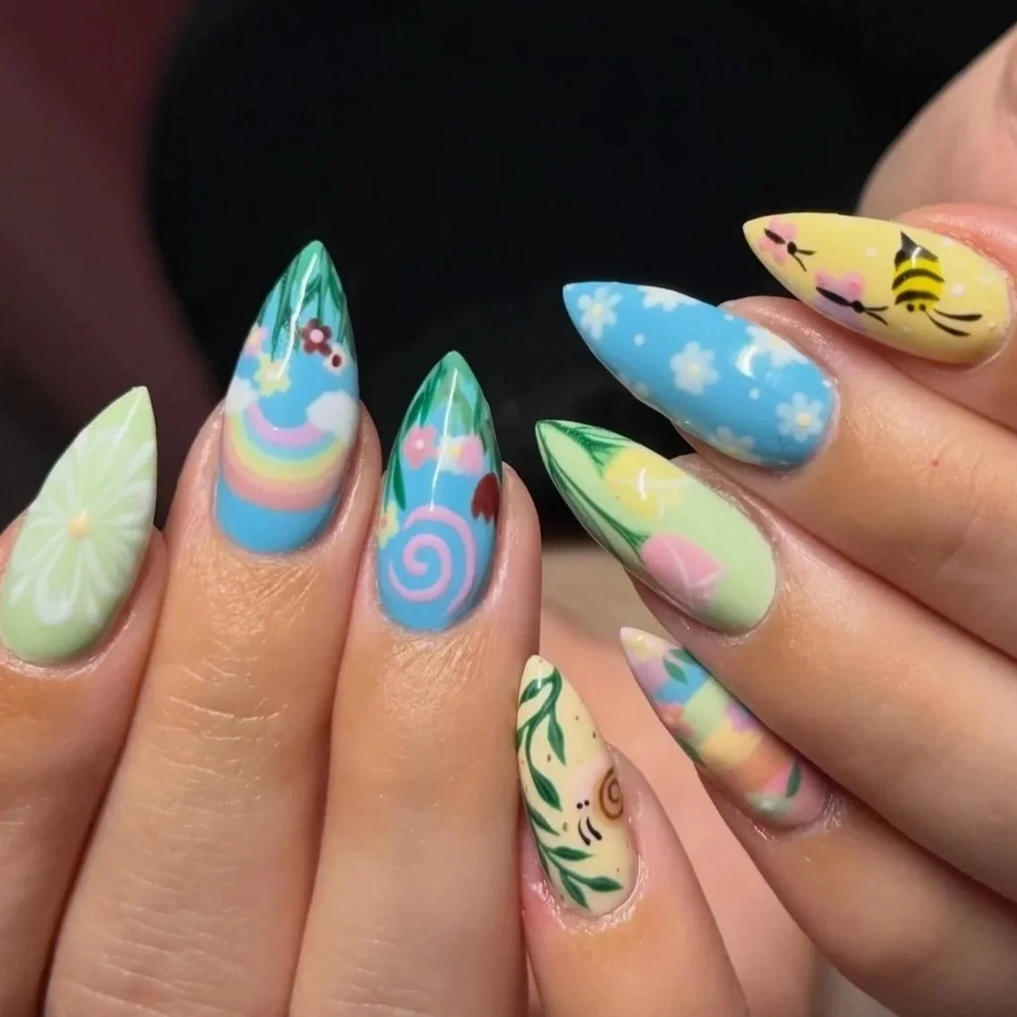 Close-up of colorful, spring-themed nail art with floral and nature designs on long, pointed nails.
