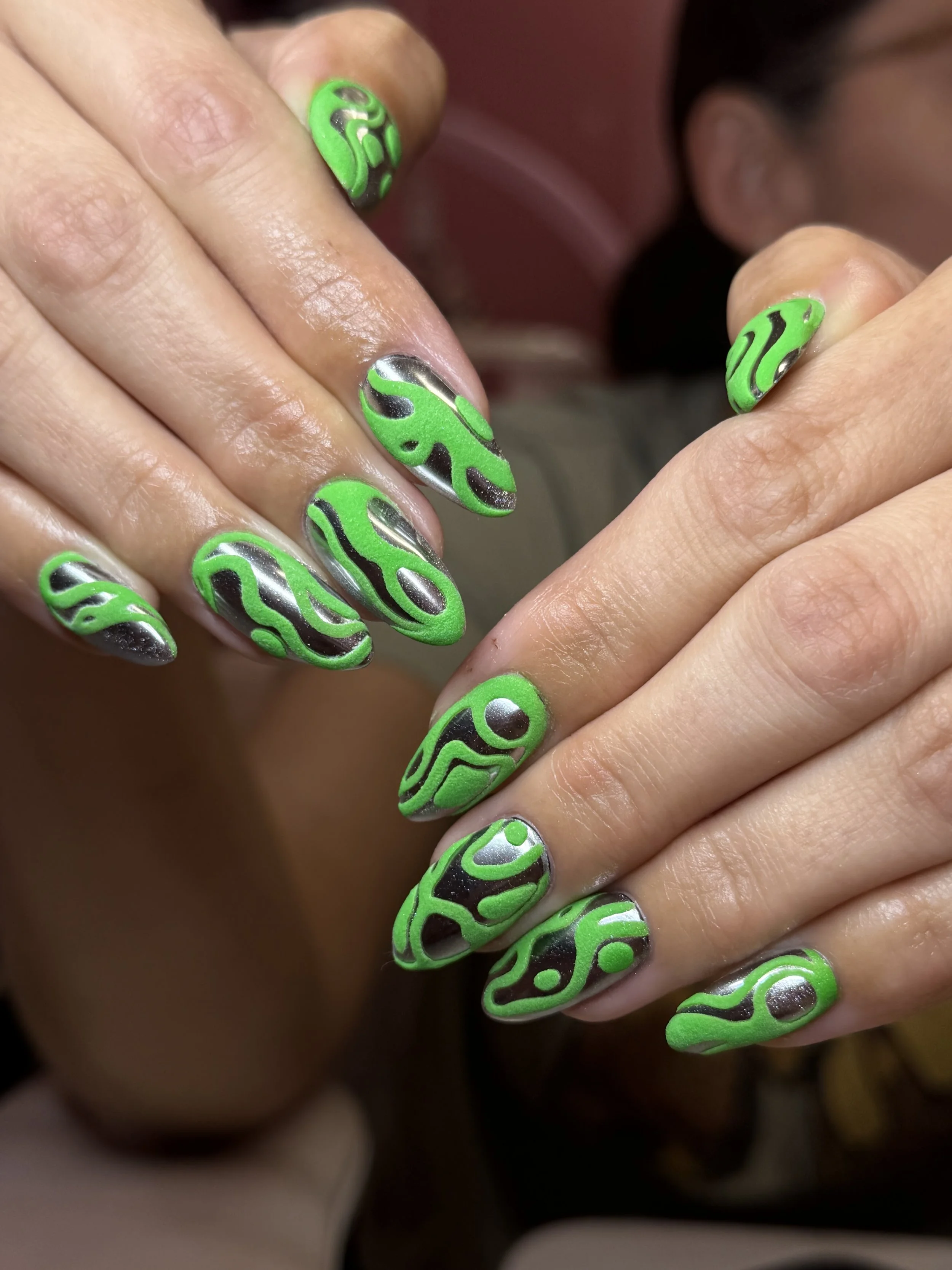 Close-up of hands with brightly colored, abstract green and black patterned nail art.