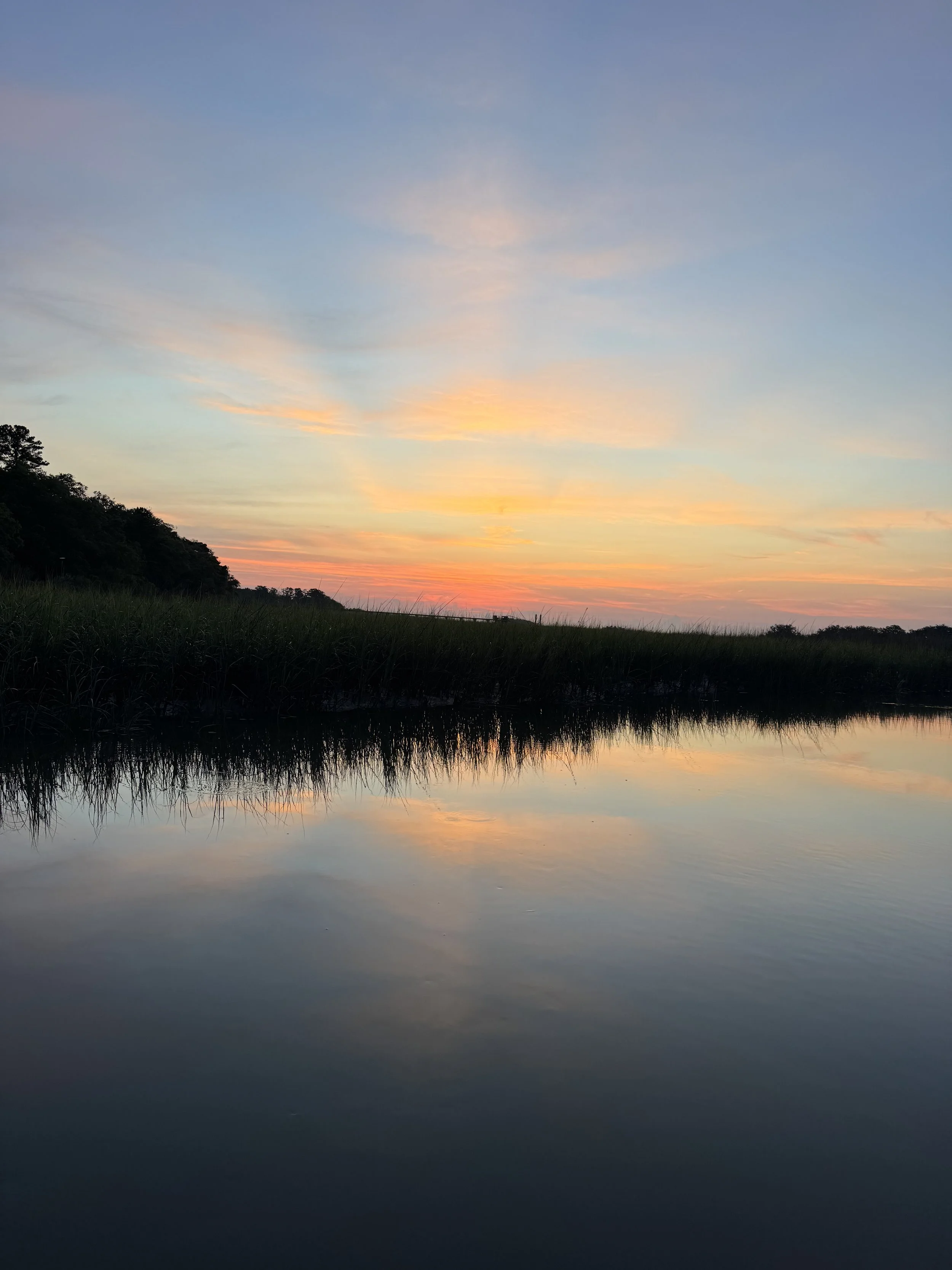 A peaceful sunrise over the Harbor River with silhouetted trees lining in the distance.