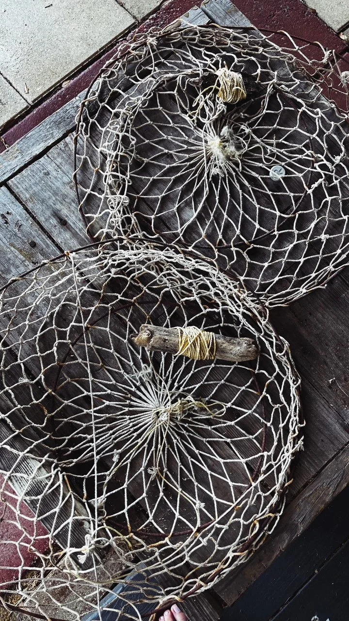 Two vintage fishing nets with wooden handles resting on a wooden surface.