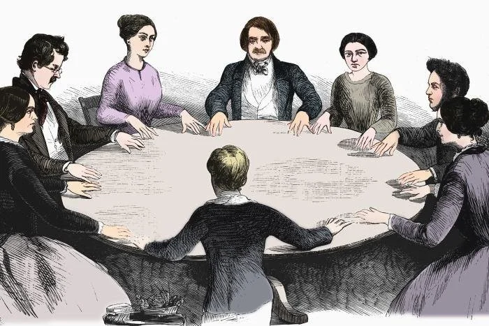 Historical illustration of a group of nine people sitting around a large round table, engaged in a meeting or discussion.