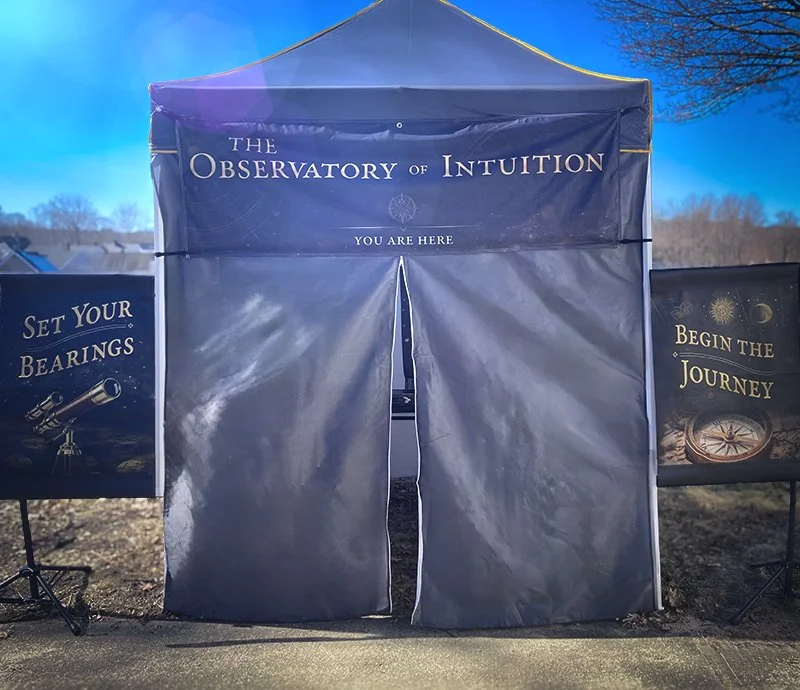A large blue tent with the words "The Observatory of Intuition" and "You Are Here" written on it. On either side, there are signs with the phrases "Set Your Bearings" and "Begin the Journey," featuring images of a telescope and a compass.