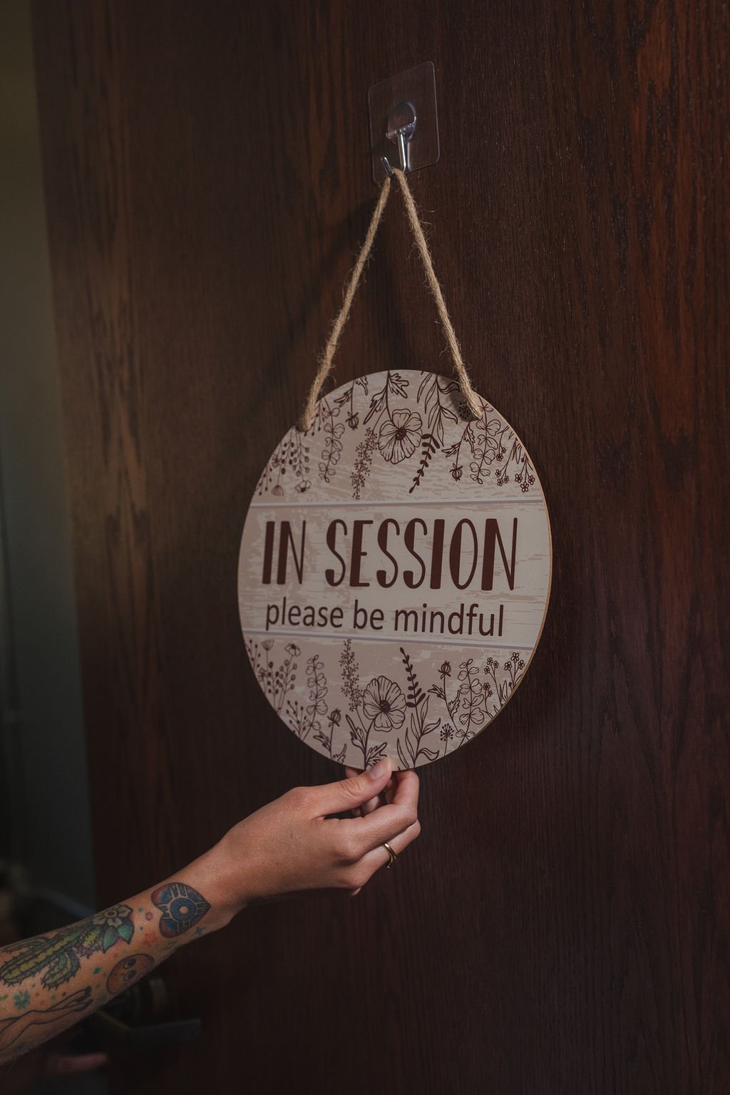 A decorative door sign on a Wichita therapists office saying "In Session, please be mindful". The door sign is round wth wildflower designs.