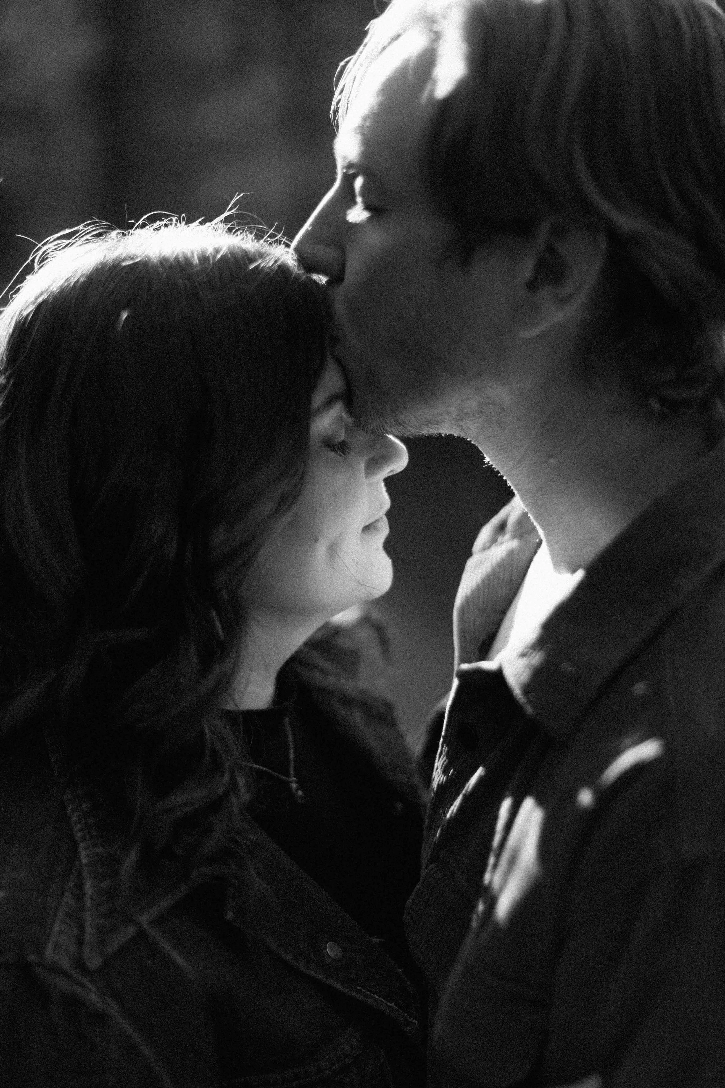 A black and white photograph of a man and woman in an intimate moment, with the man kissing the woman's forehead and the woman closing her eyes.