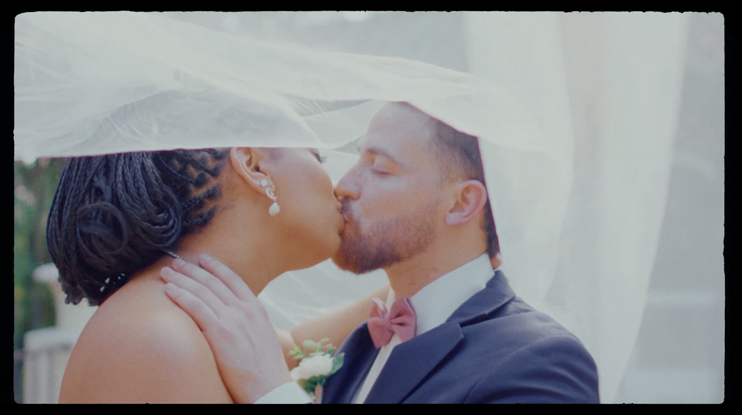 A bride and groom sharing a kiss under a white veil during their wedding ceremony.