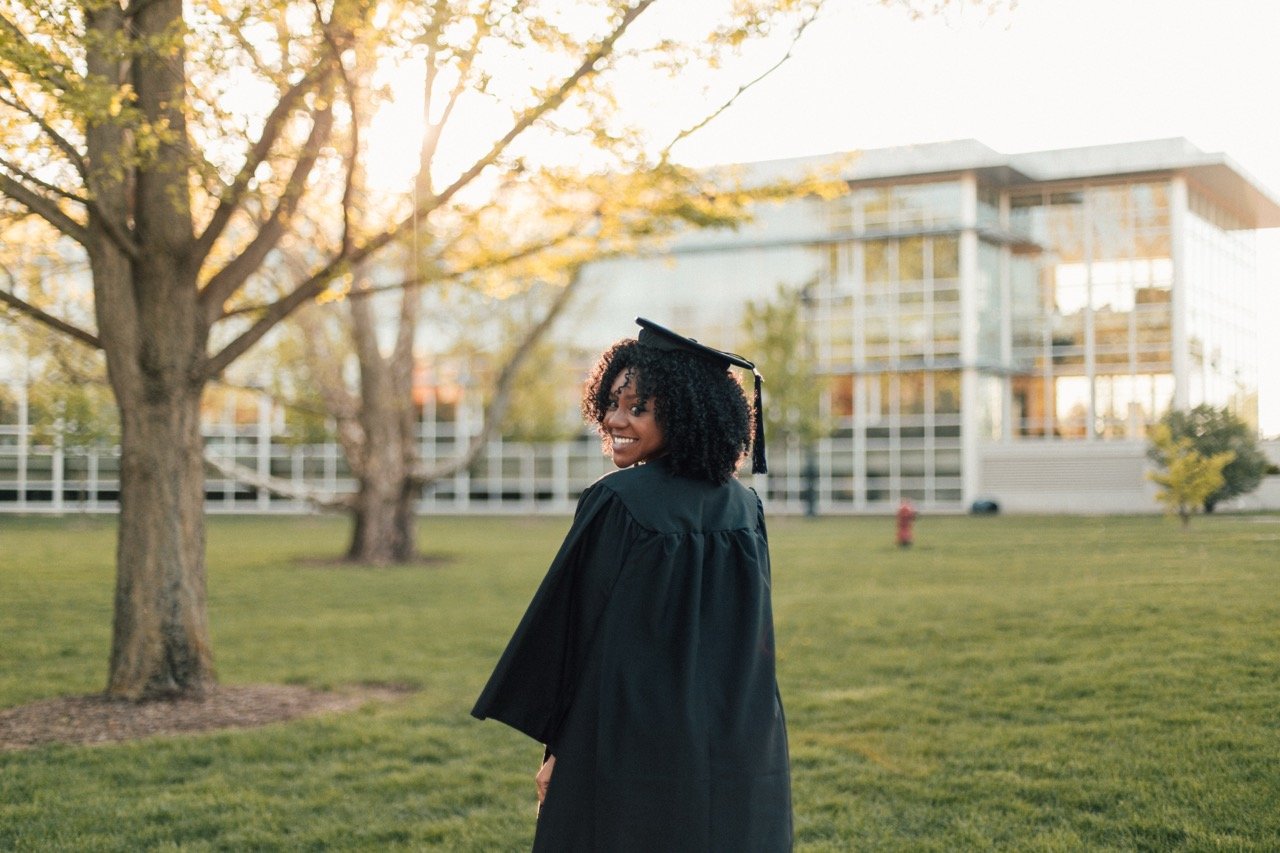 Young woman in graduation gown and cap smiling outdoors