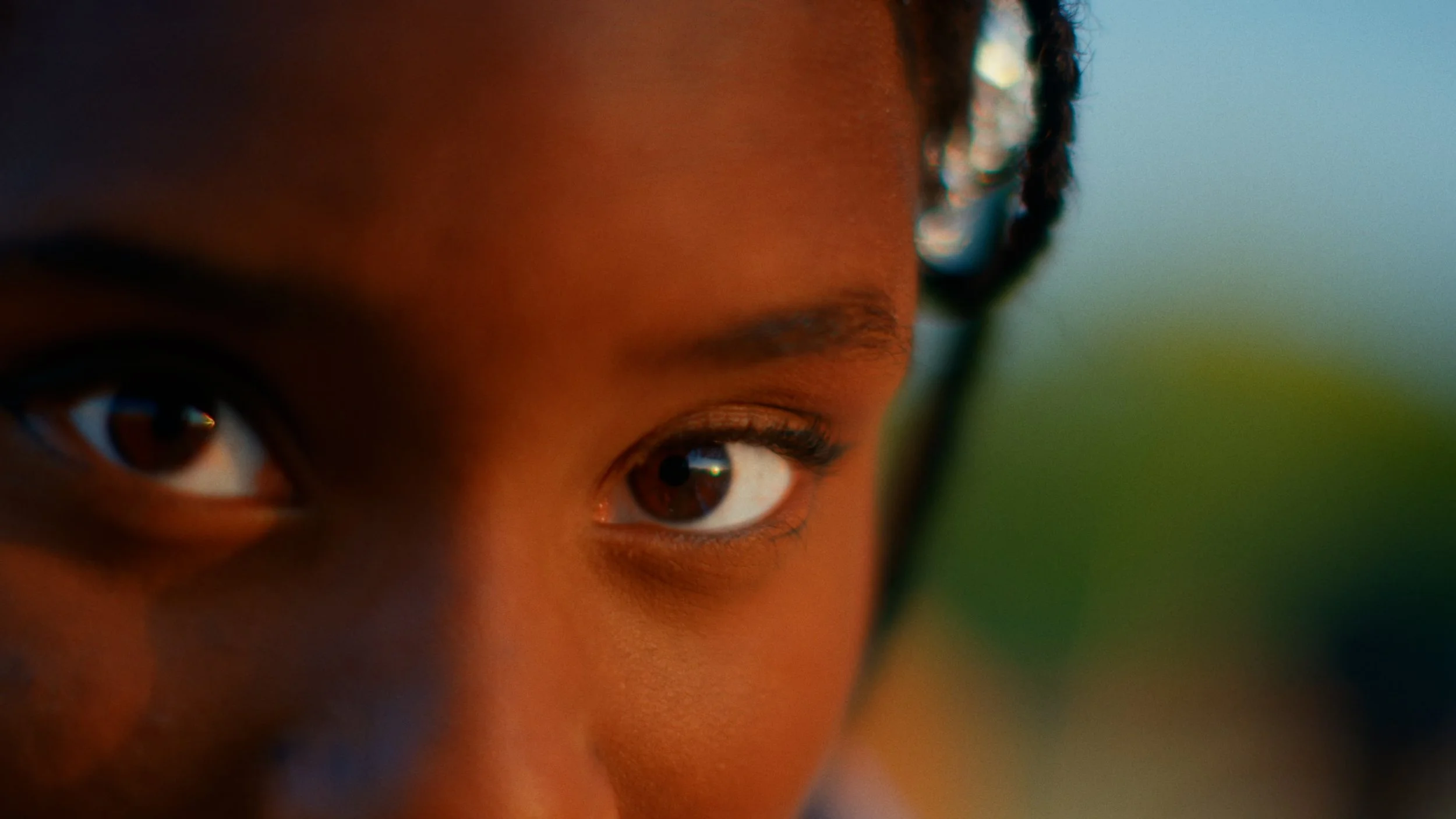 Close-up of a person's face focused on their eyes, with a blurred background and reflective glasses.