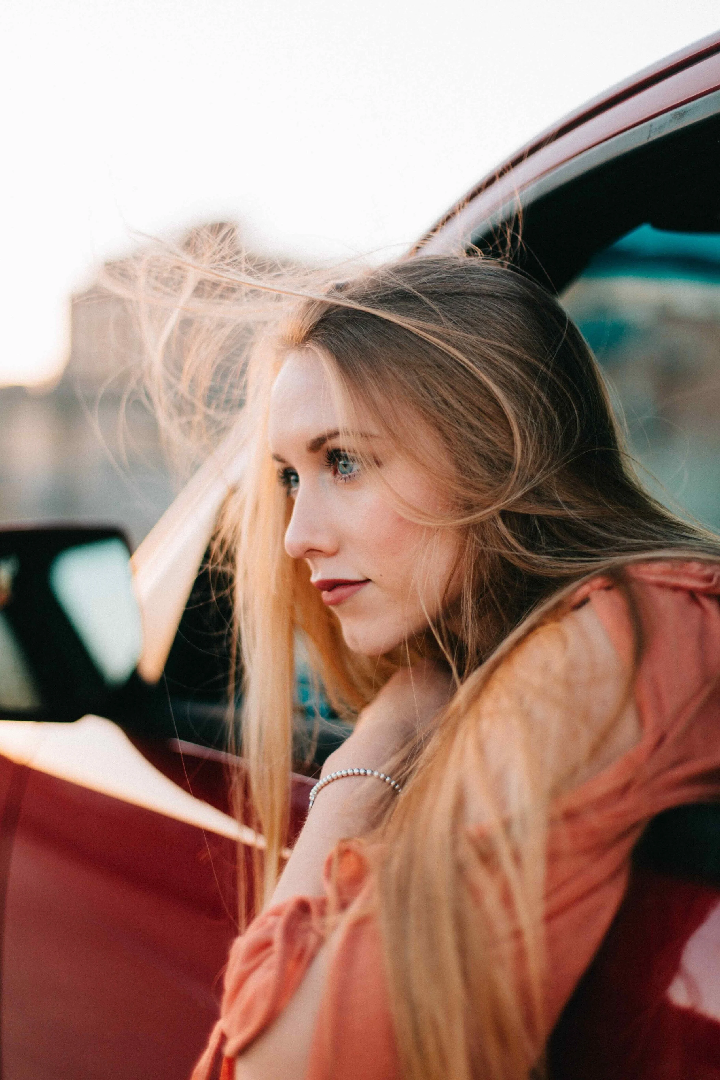 Close-up of a woman with long, blonde hair, sitting in a car, looking at her phone with wind blowing her hair.