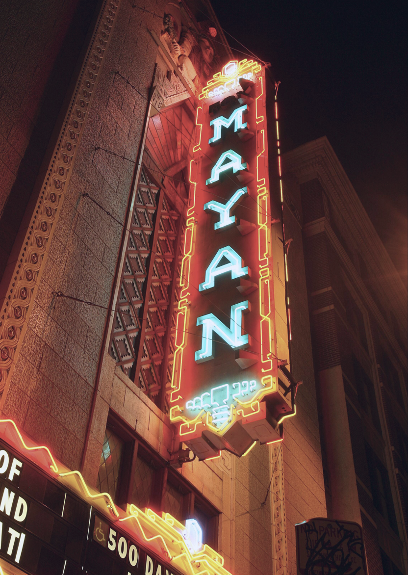 Nighttime neon sign reading 'MAYAN' in blue and red neon lights on a tall building.