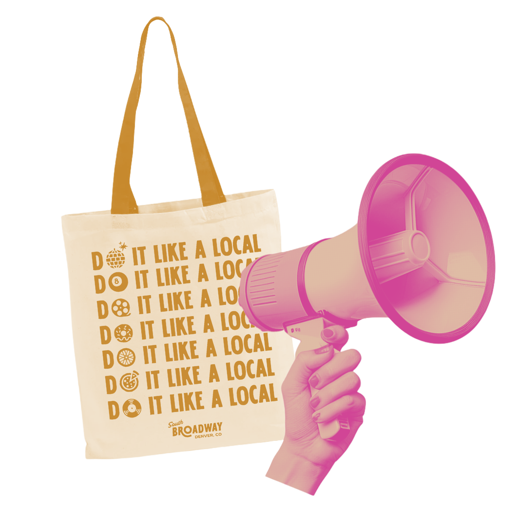 A beige tote bag with bold brown text and symbols, and a pink megaphone. The bag displays the phrase "Do it like a local" repeatedly with various icons representing local themes, and locates South Broadway in Denver, CO.