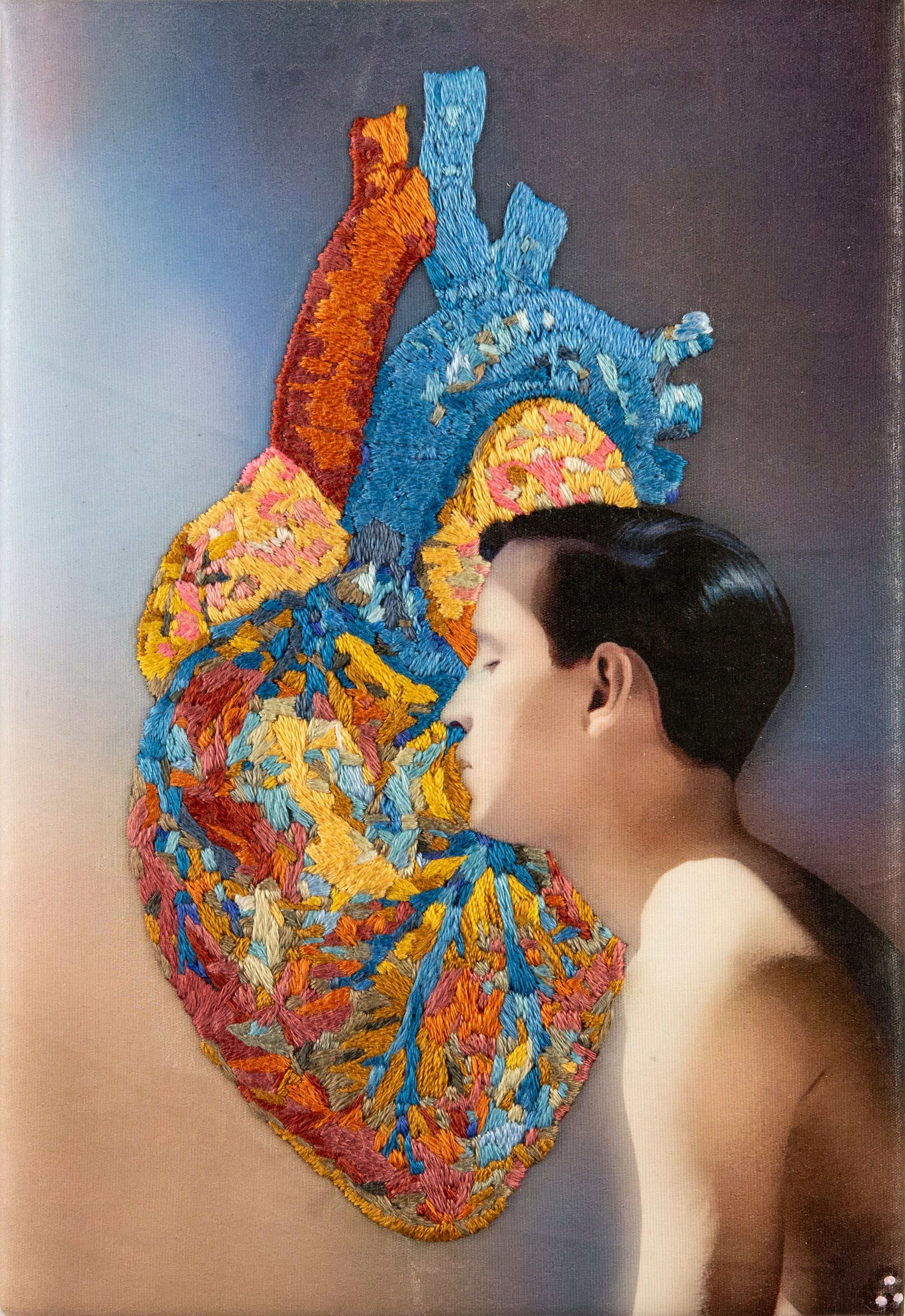 A male profile emerges from within an embroidered heart in blues, reds, and gold. Hand-embroidered queer art by Vancouver artist Paul Gravett.