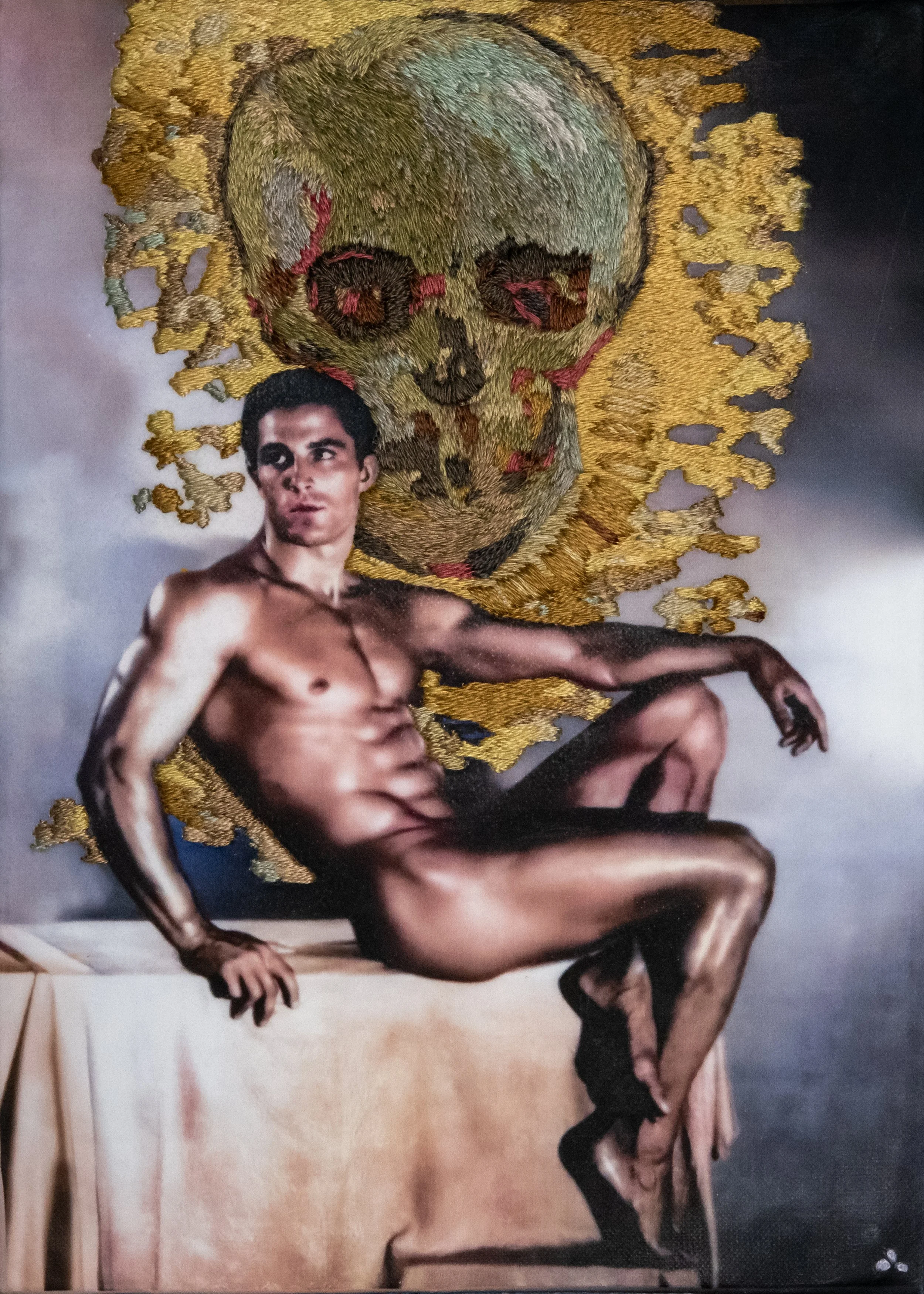 Description: Tony Sansone reclines as Van Gogh's skull, embroidered in gold and ochre, looms above — a vanitas for gay men lost to time. Queer art by Paul Gravett.
