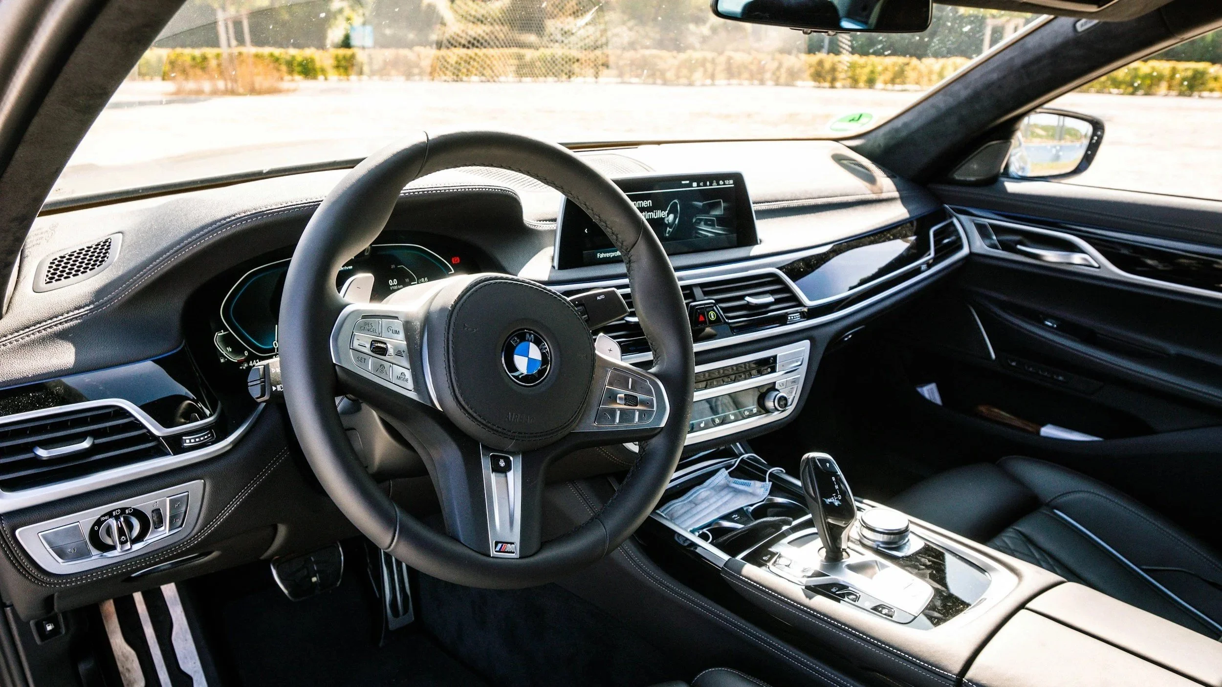 Interior view of a BMW car dashboard with a BMW steering wheel, digital instrument cluster, center display screen, and various control buttons and panels.