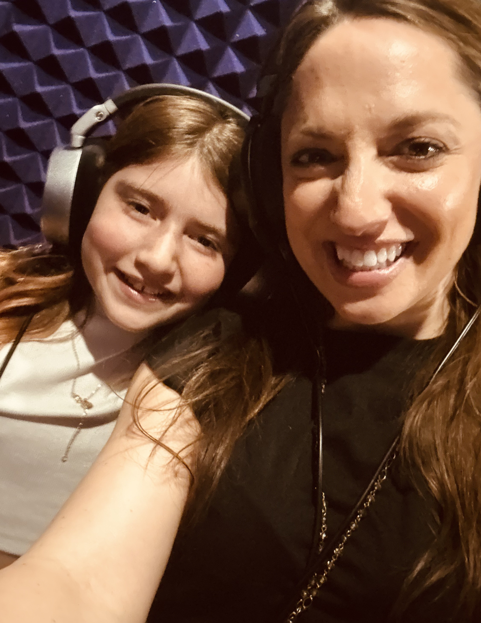 Close-up of two women smiling, one wearing headphones, in a recording studio with soundproof foam panels in the background.