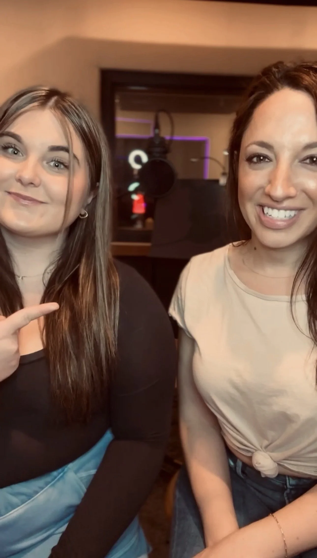 Two women smiling and sitting close together in what appears to be a recording studio or similar space.