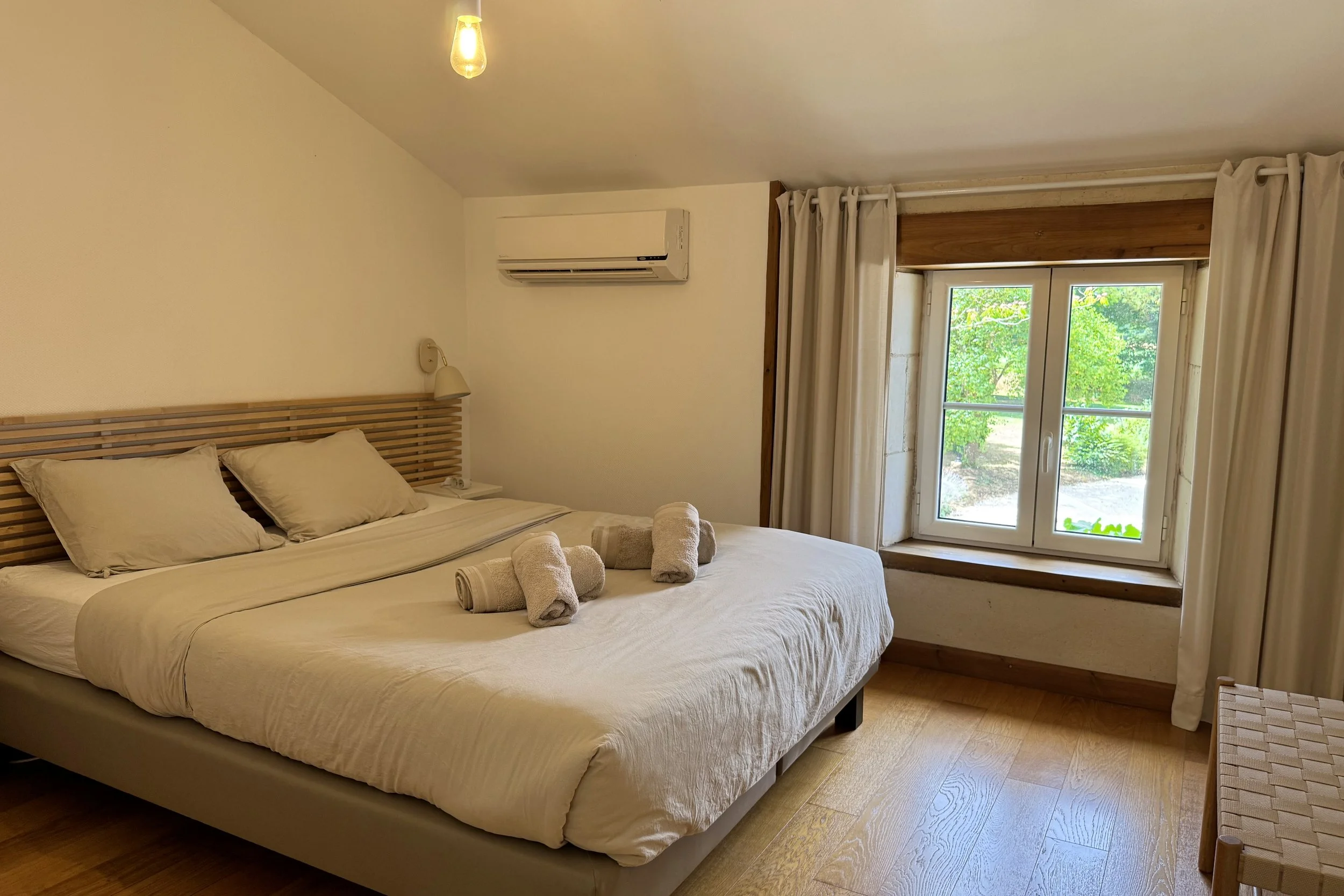 Chambre avec lit double, serviettes pliées, fenêtre avec vue sur la nature, et Air Conditioner.