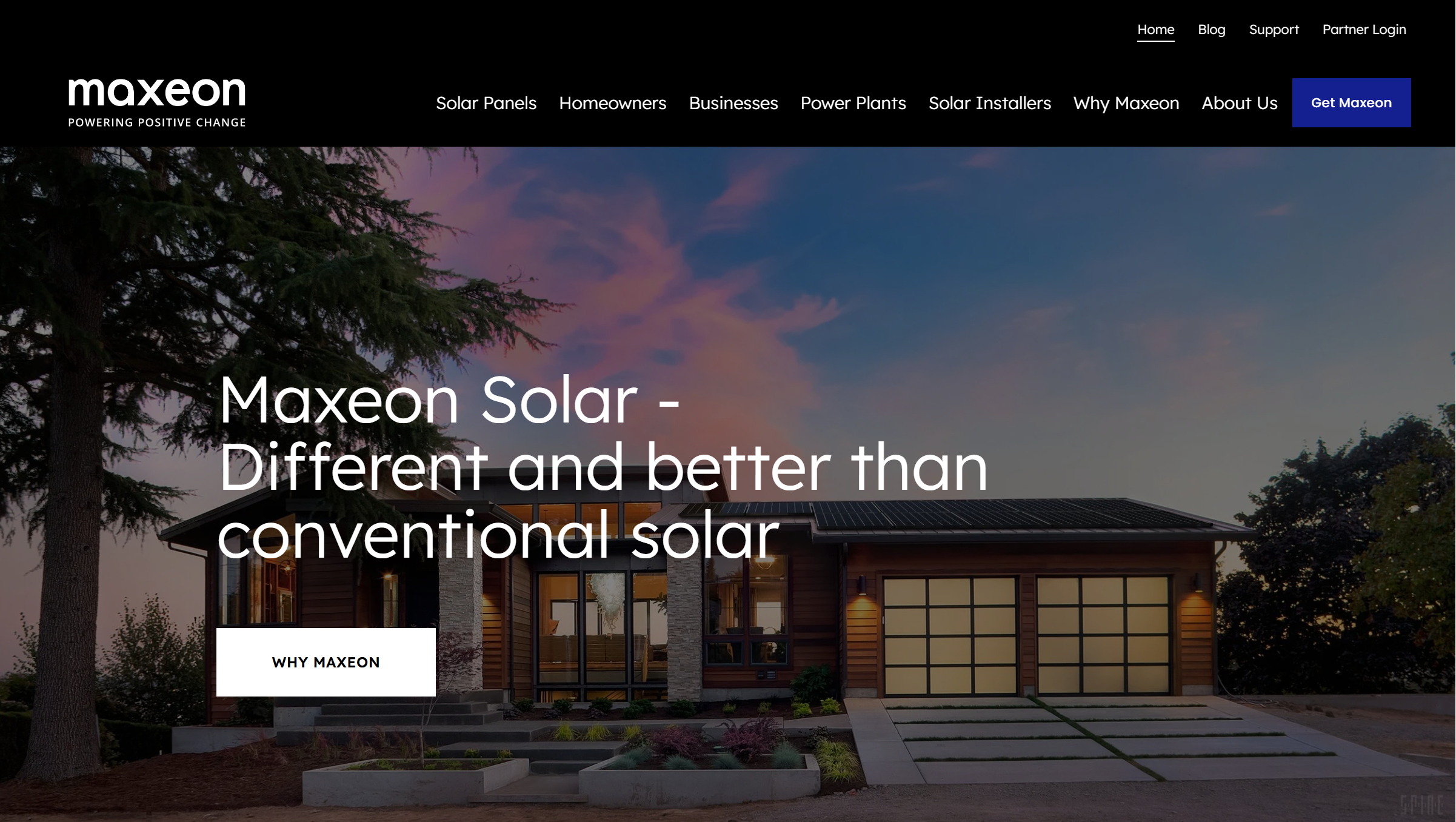 A modern house with solar panels on the roof, trees, and a landscaped front yard during sunset.