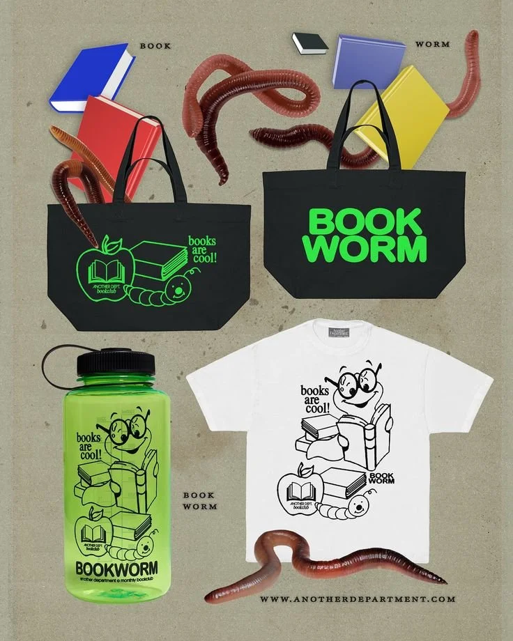 Collection of book-themed items including two black tote bags, a white t-shirt, a green water bottle, and several worm props, all featuring worm and book illustrations with the phrase "books are cool!" and the brand name "Book Worm".