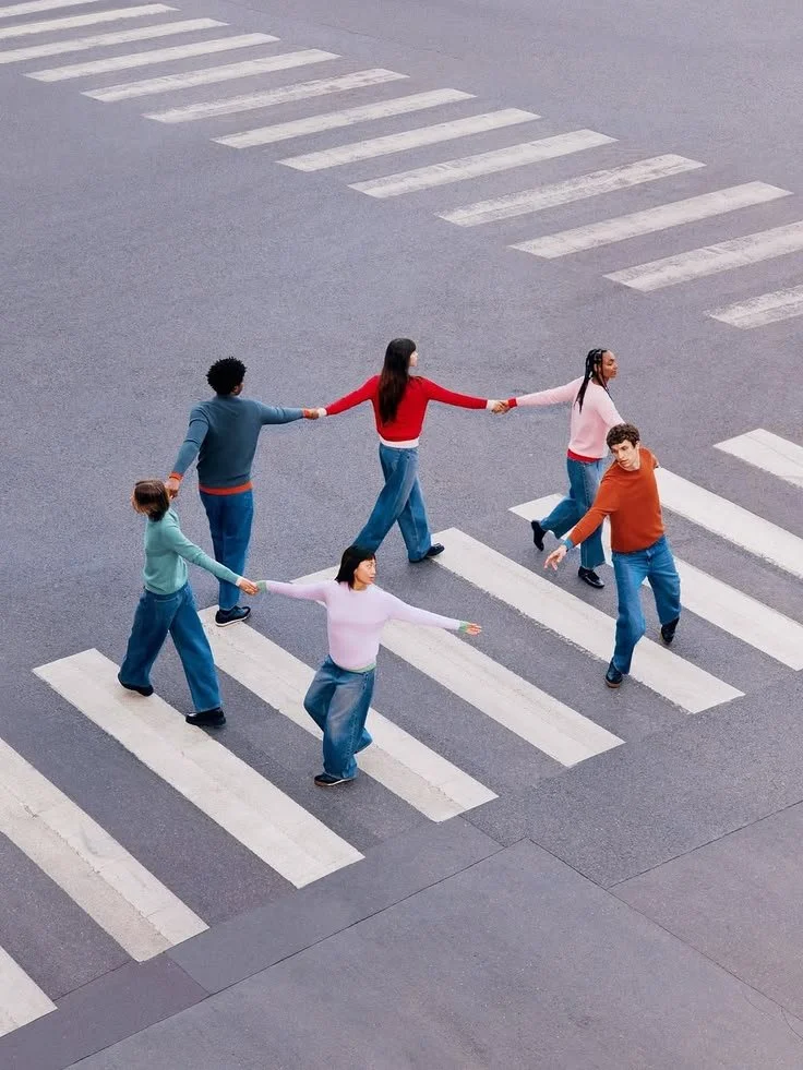 A group of six people holding hands and walking across a crosswalk on a city street.
