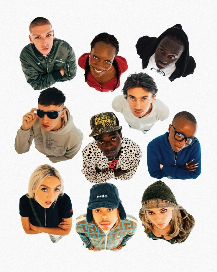 A group of eleven diverse young adults looking up at the camera with various expressions, standing close together against a white background.