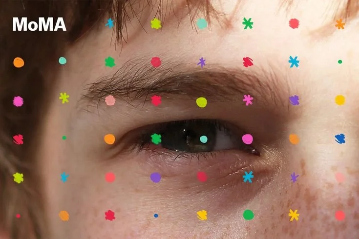Close-up of a person's eye surrounded by colorful confetti-like spots and the MoMA logo in the top left corner.