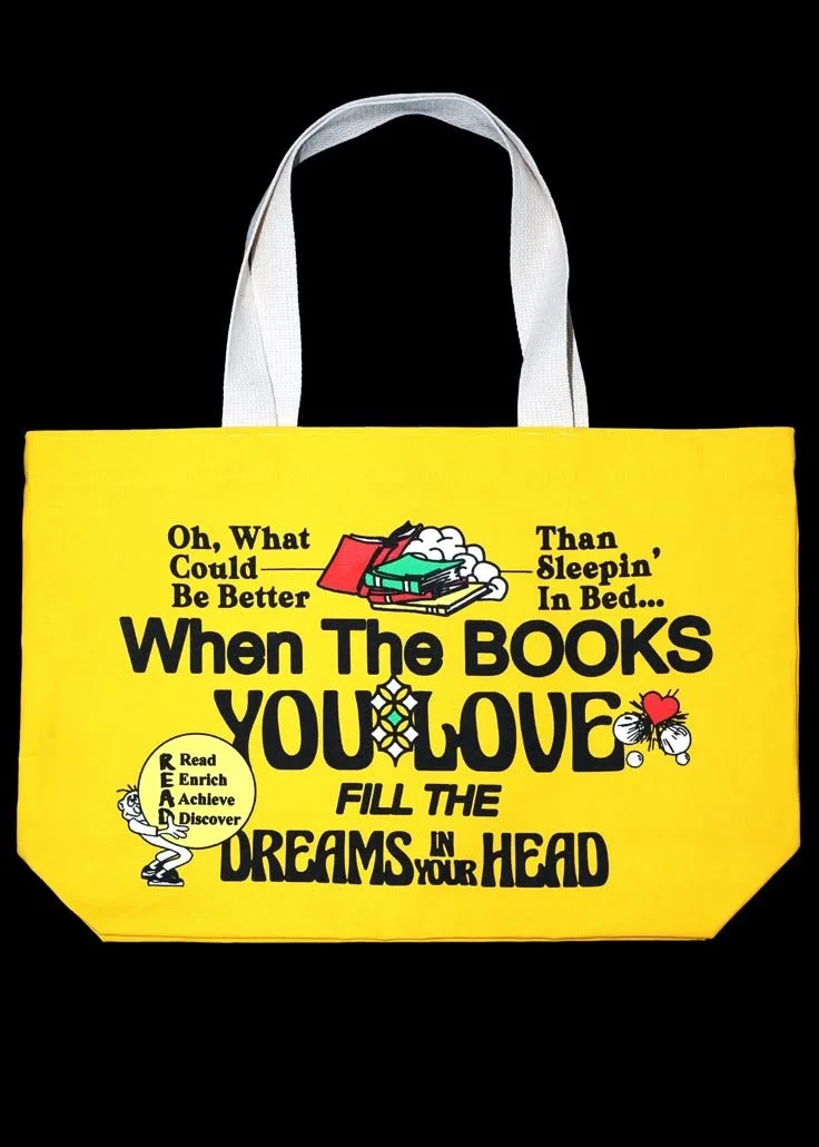 Yellow tote bag with black text and illustrations, featuring books and a butterfly, with a white handle.