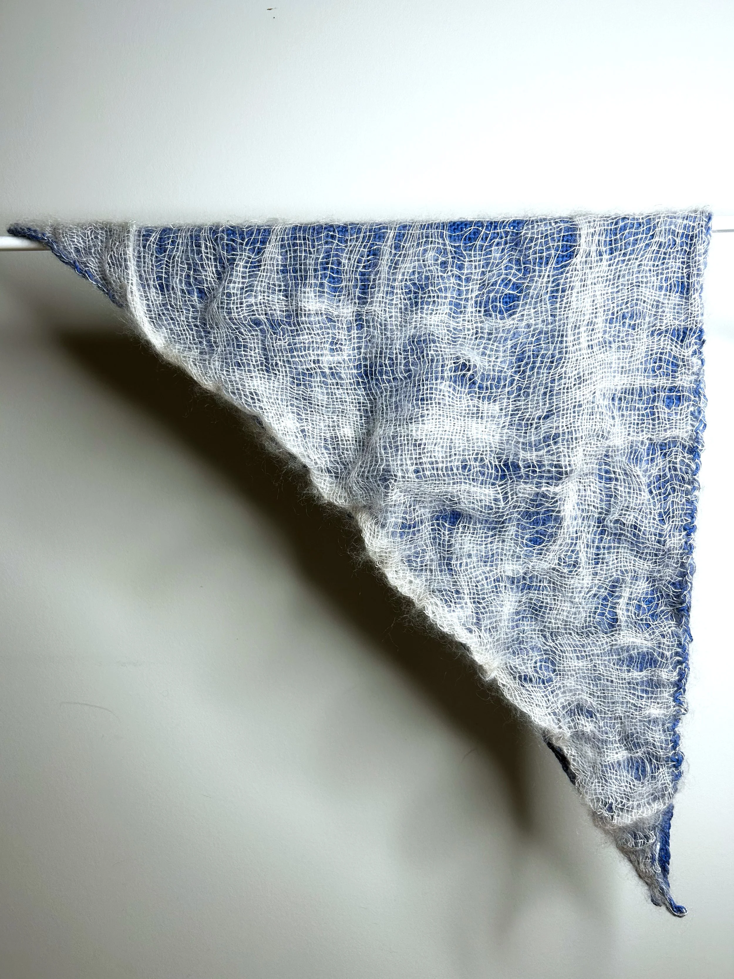 Ein blaues handgewebtes Dreieckstuch, das auf einem Stab hängt.