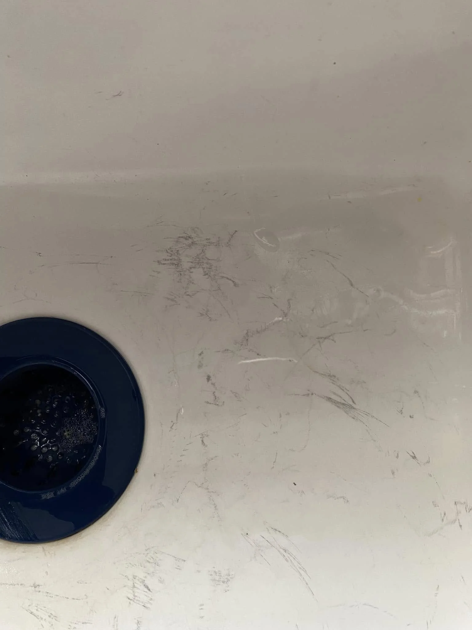 A white table with scratches and marks, and a dark blue round object, possibly a drain or part of a sink, located in the bottom left corner.