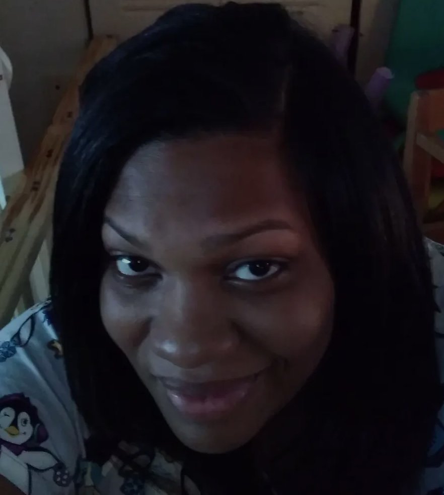 A woman with dark hair and a bright smile looking up at the camera in a dimly lit room.