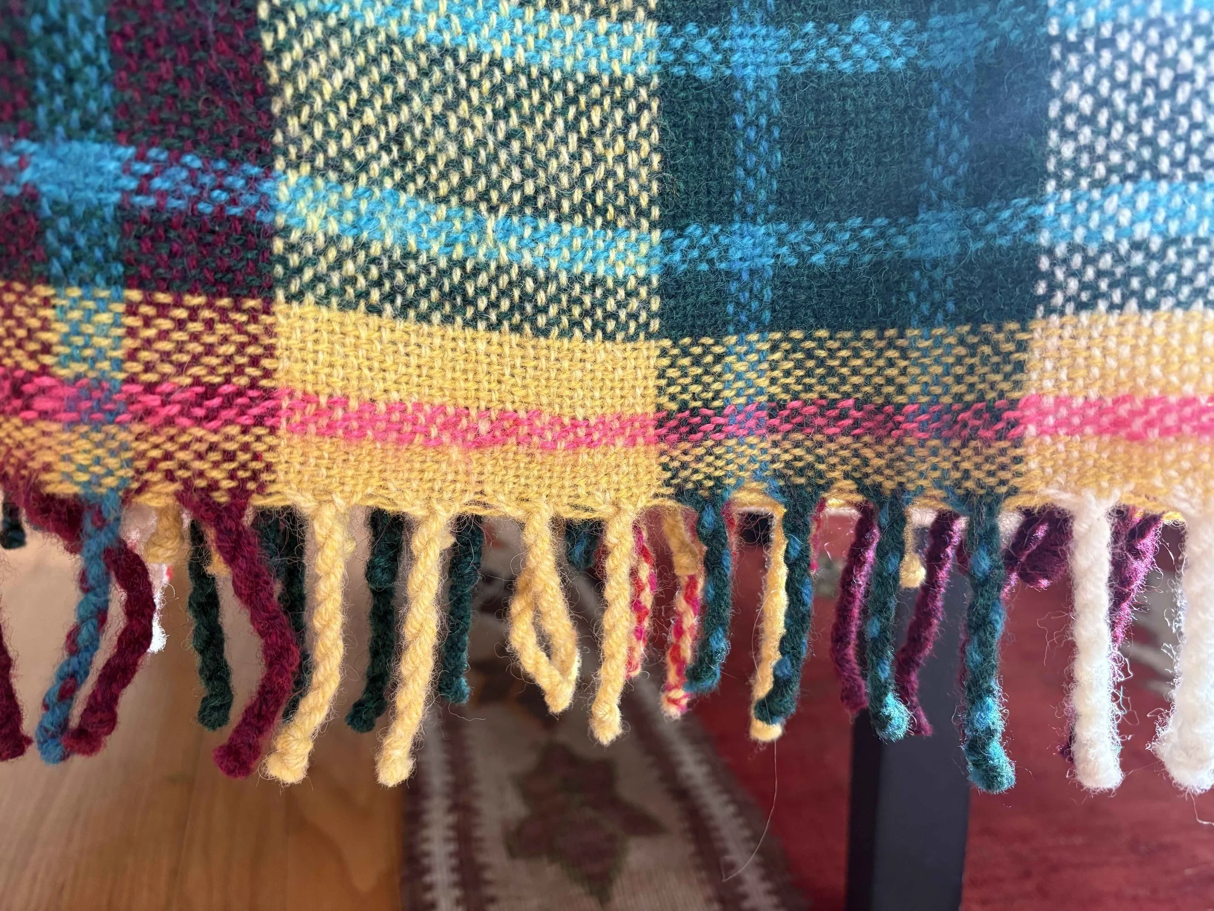Close-up of a multicolored woven textile with fringes, featuring pink, yellow, blue, green, and black threads.