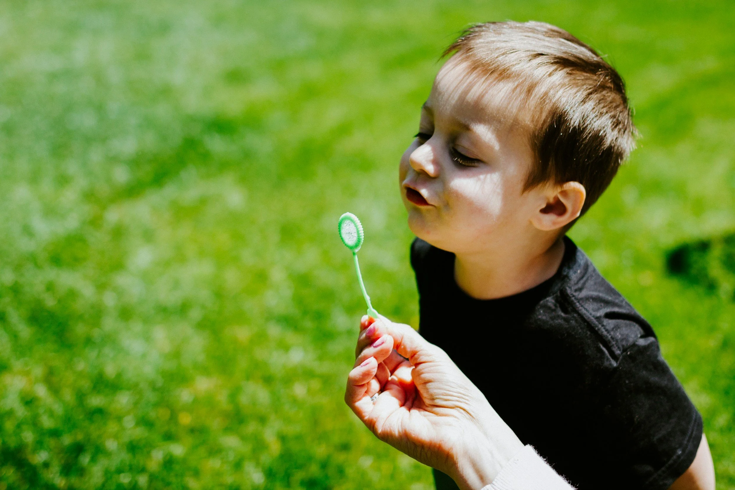 Young boy engaging in speech therapy outdoors and blowing bubbles in a park with green grass and sunlight.