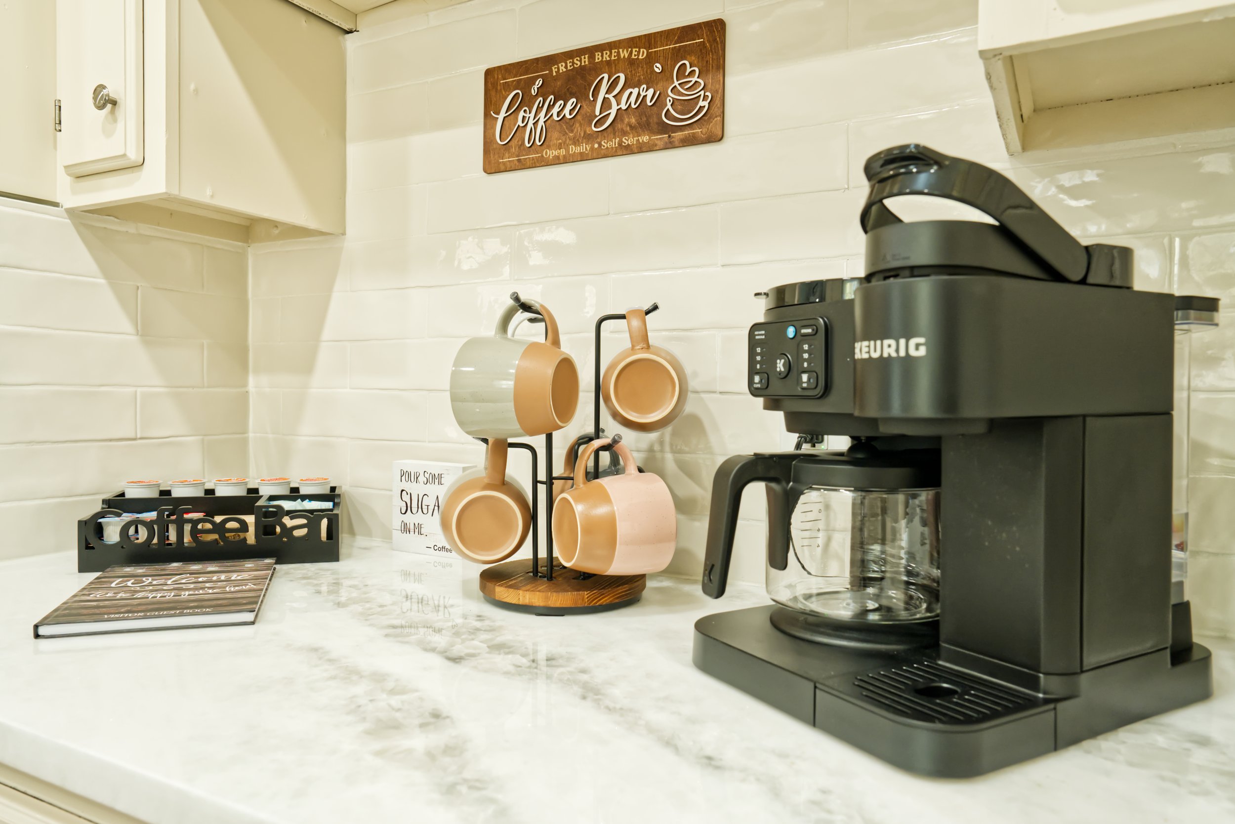 A coffee station with a Keurig coffee maker, cups hanging on a rack, a sign that says 'Coffee Bar,' and a menu on the counter.