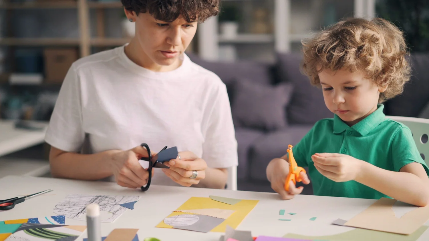 A little boy practicing cutting paper with scissors at a craft table