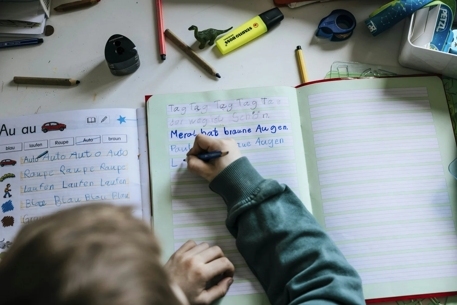 A young child practicing writing letters in a notebook with a pencil