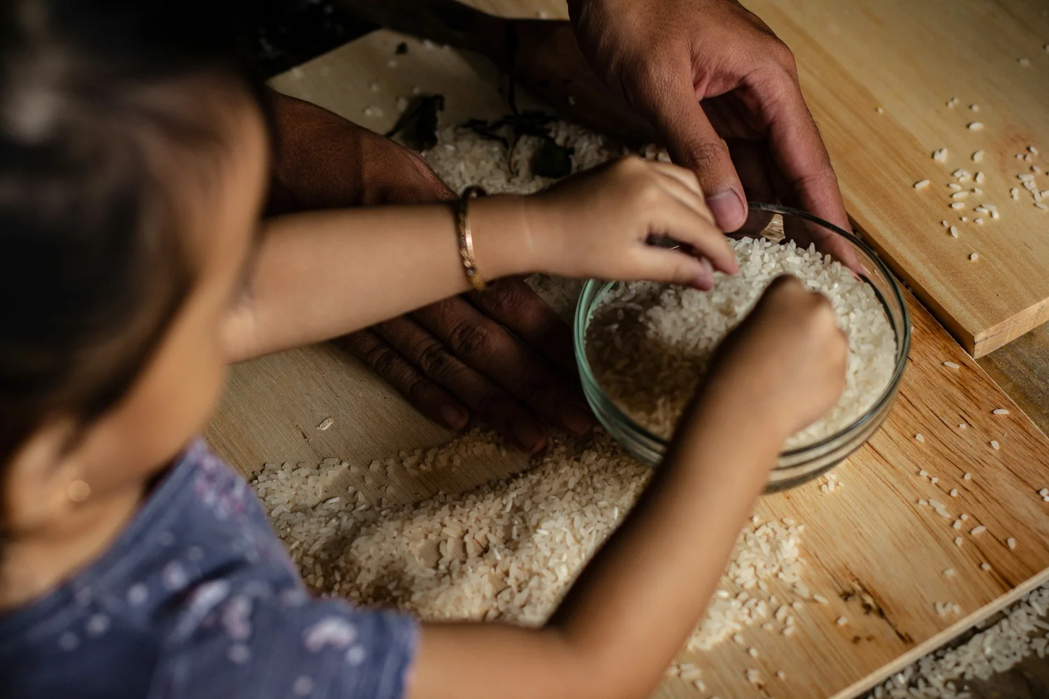 A child's hands calmly exploring a sensory bin of dry rice and scoops at a table