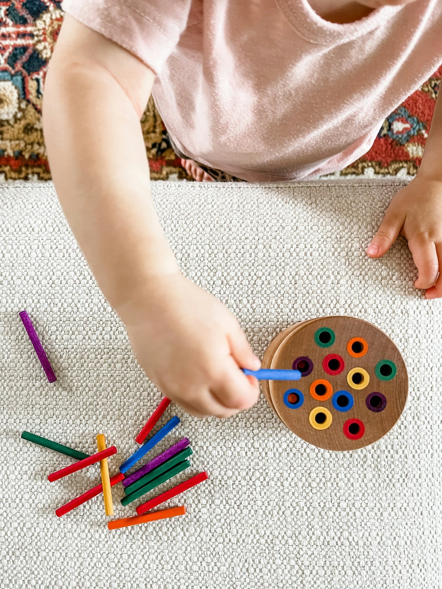 A child placing colorful sticks into a wooden pegboard — a fine motor activity at home