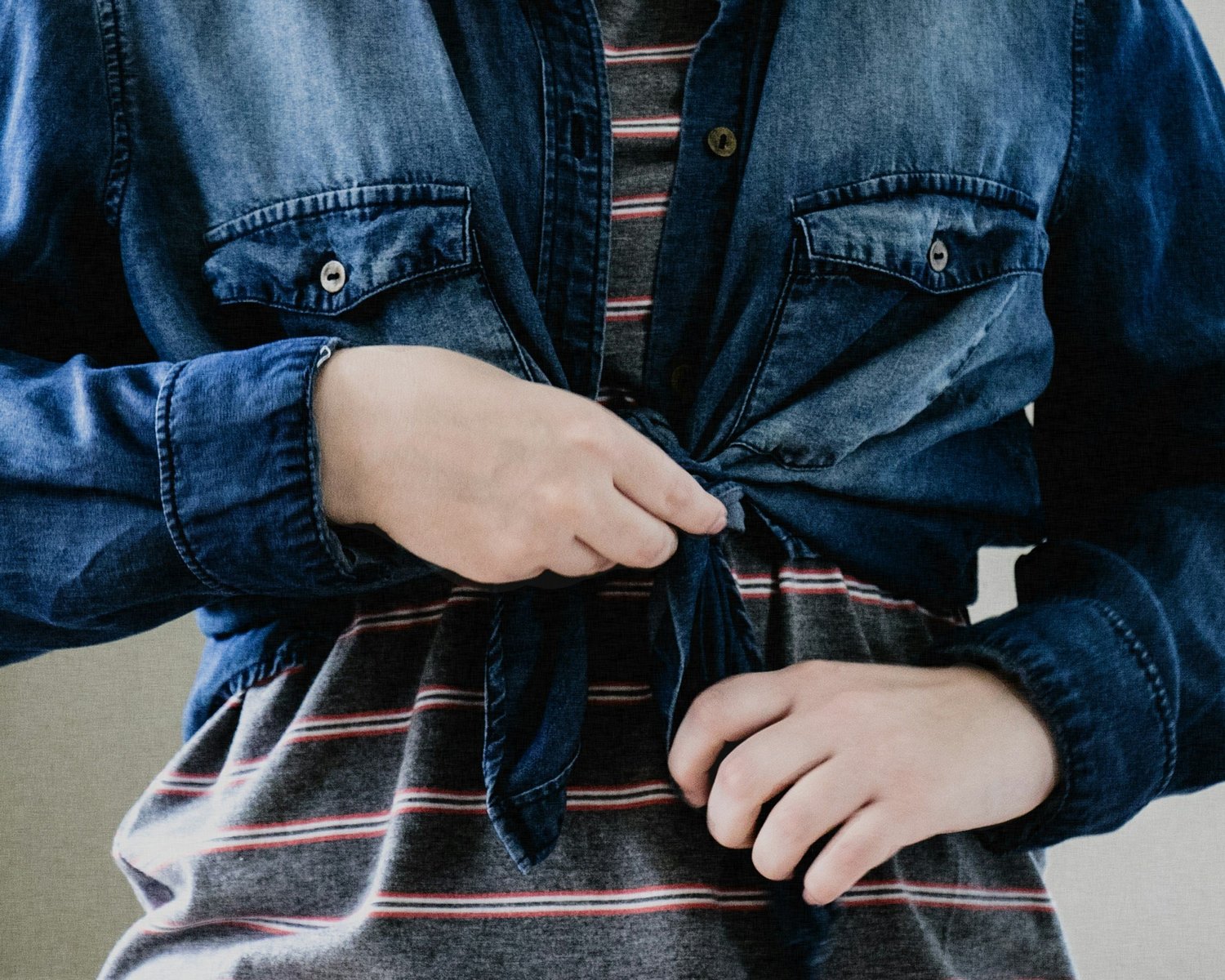 A child's hands buttoning a denim shirt while getting dressed