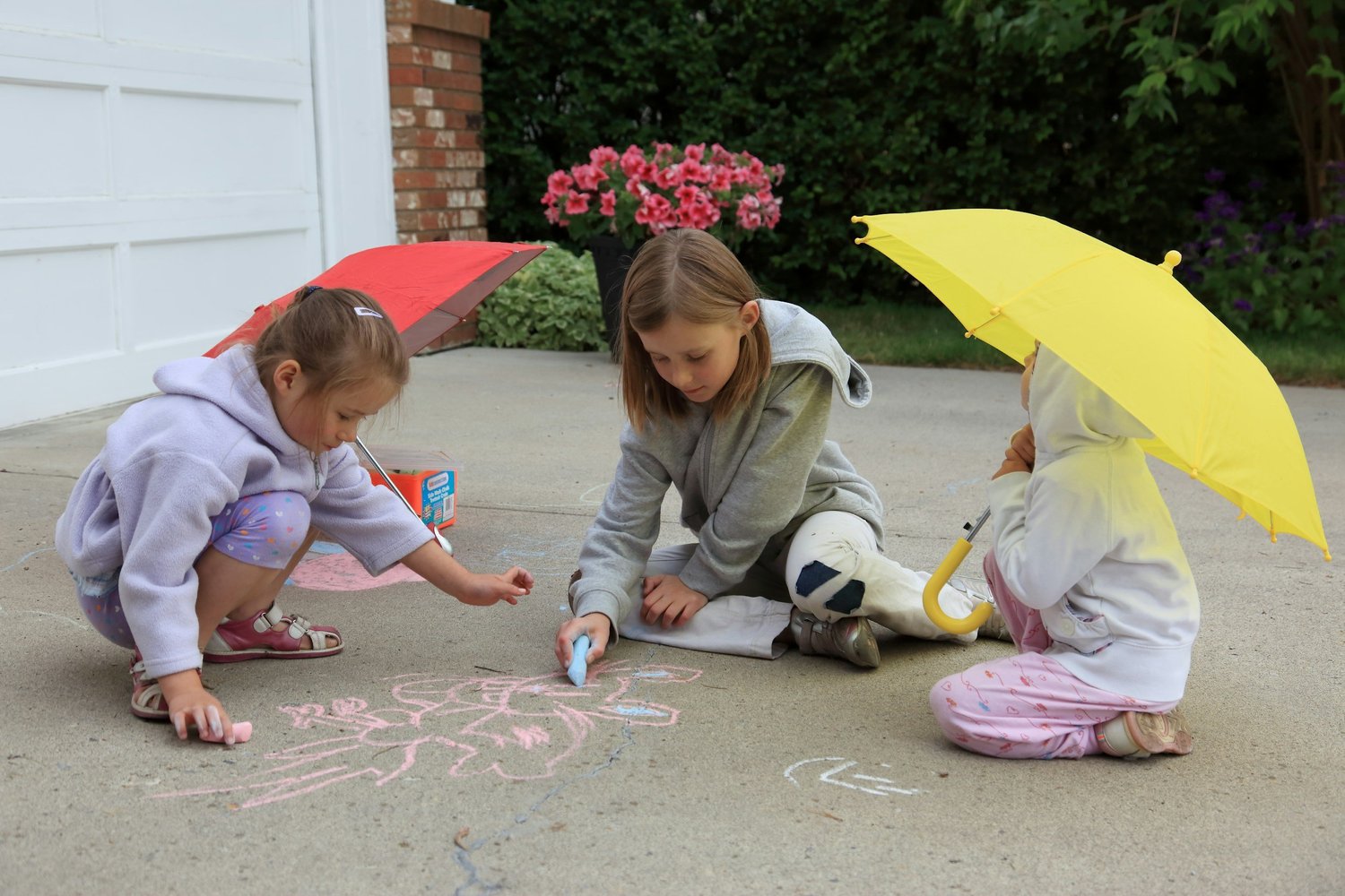 Kids drawing on the driveway with colorful sidewalk chalk on a summer day