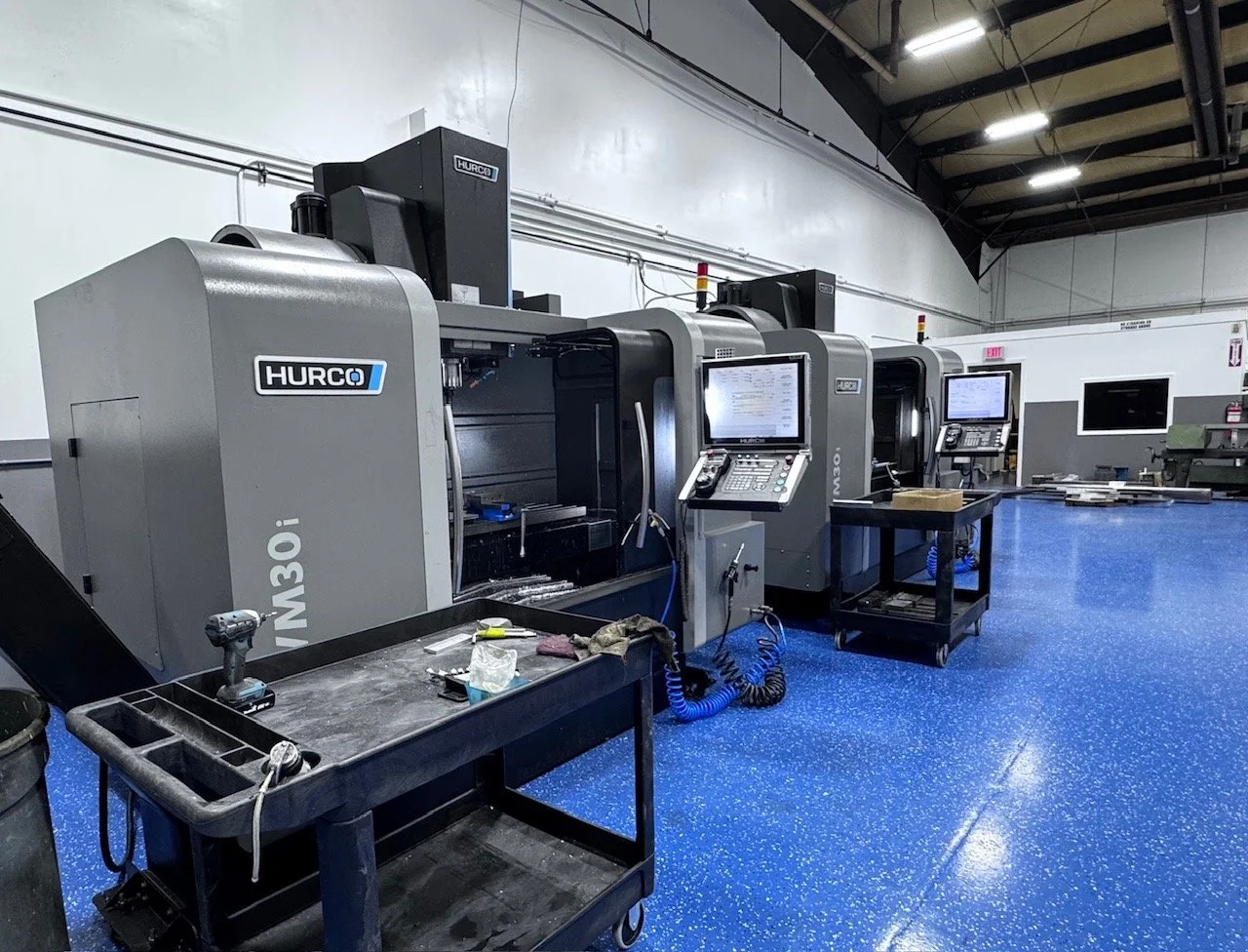 Multiple Hurco CNC machine tools in a manufacturing workshop with blue speckled floor, tool cart, and computer monitors.