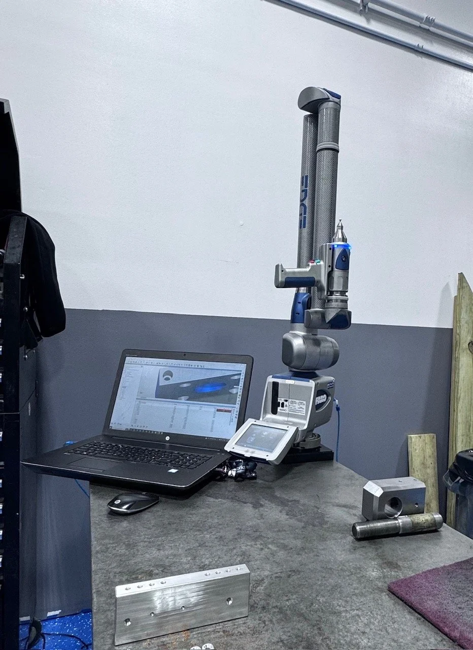 Industrial robotic arm with a computer and monitor on a workbench in a workshop or lab setting.