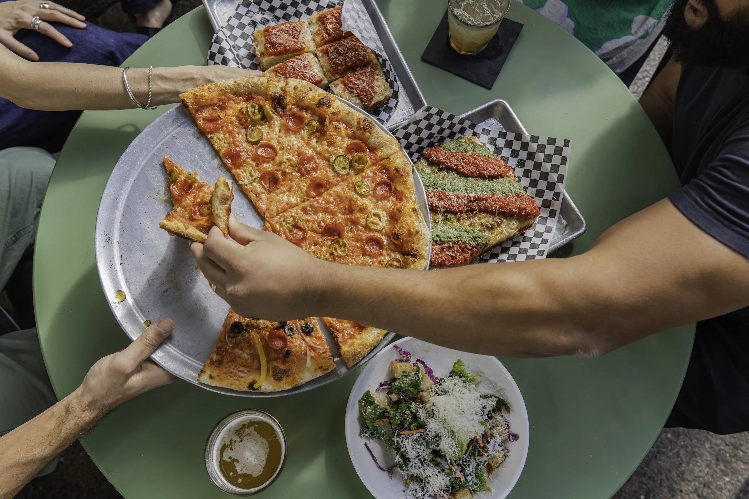Flatlay of people sharing pizza, salad, and drinks at a table at Pizza Mamo in Chinatown Honolulu.
