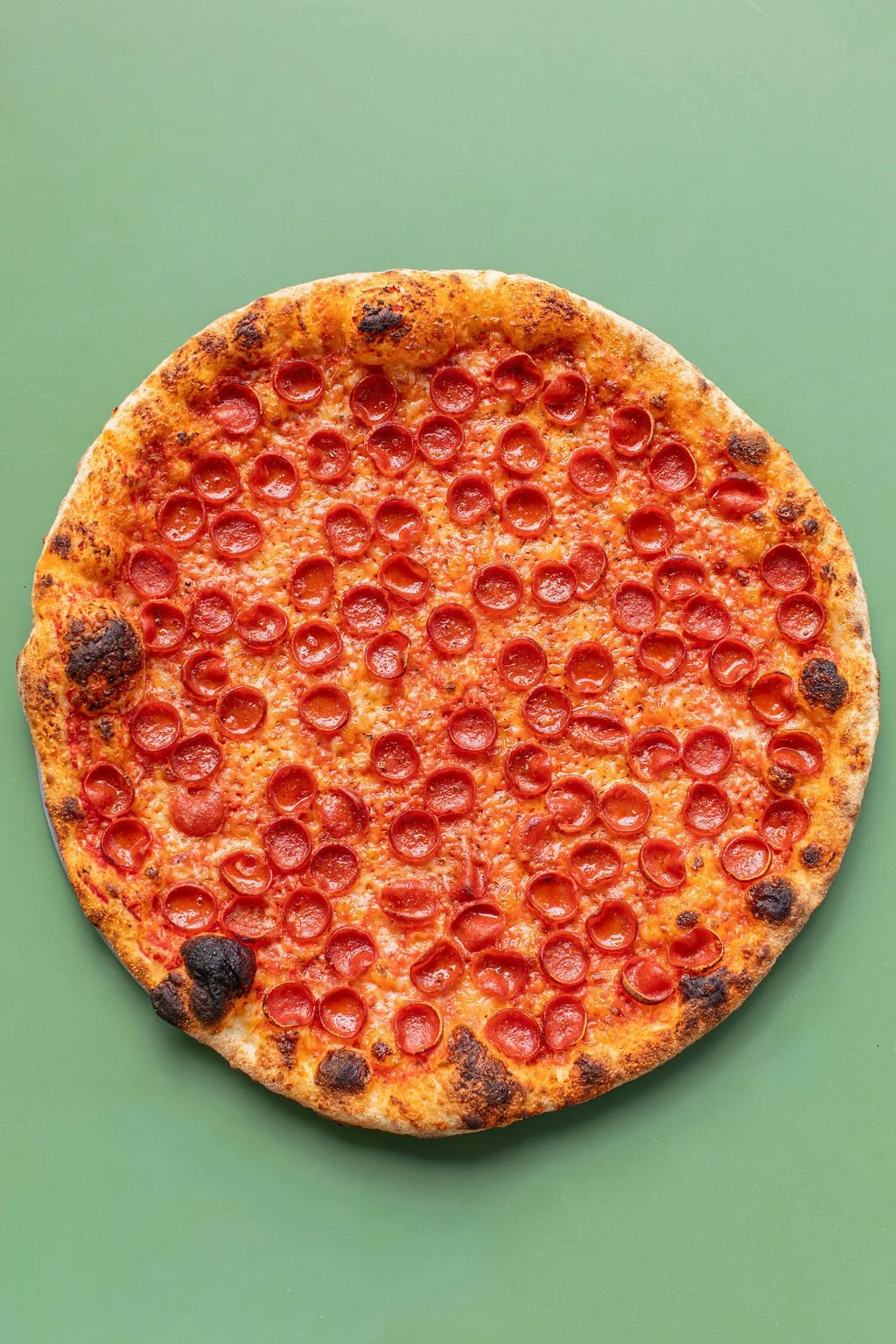 Pepperoni round image: Round pepperoni pizza on a green background from Pizza Mamo