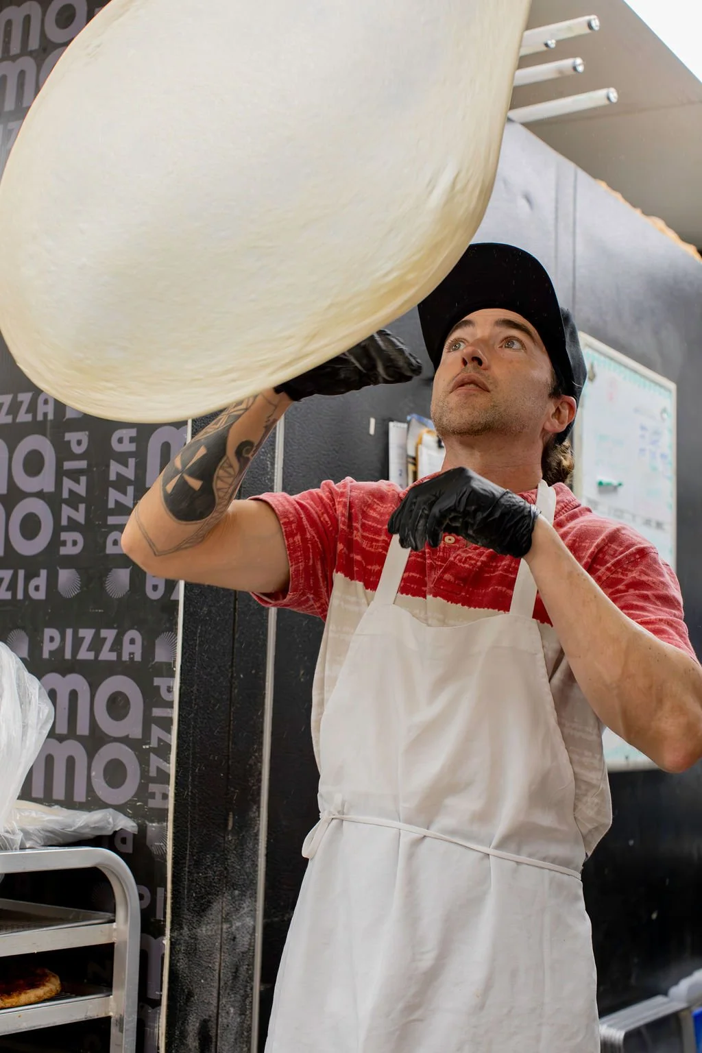 Dough toss image: Pizza Mamo team member tossing 4 day fermented pizza dough in the kitchen