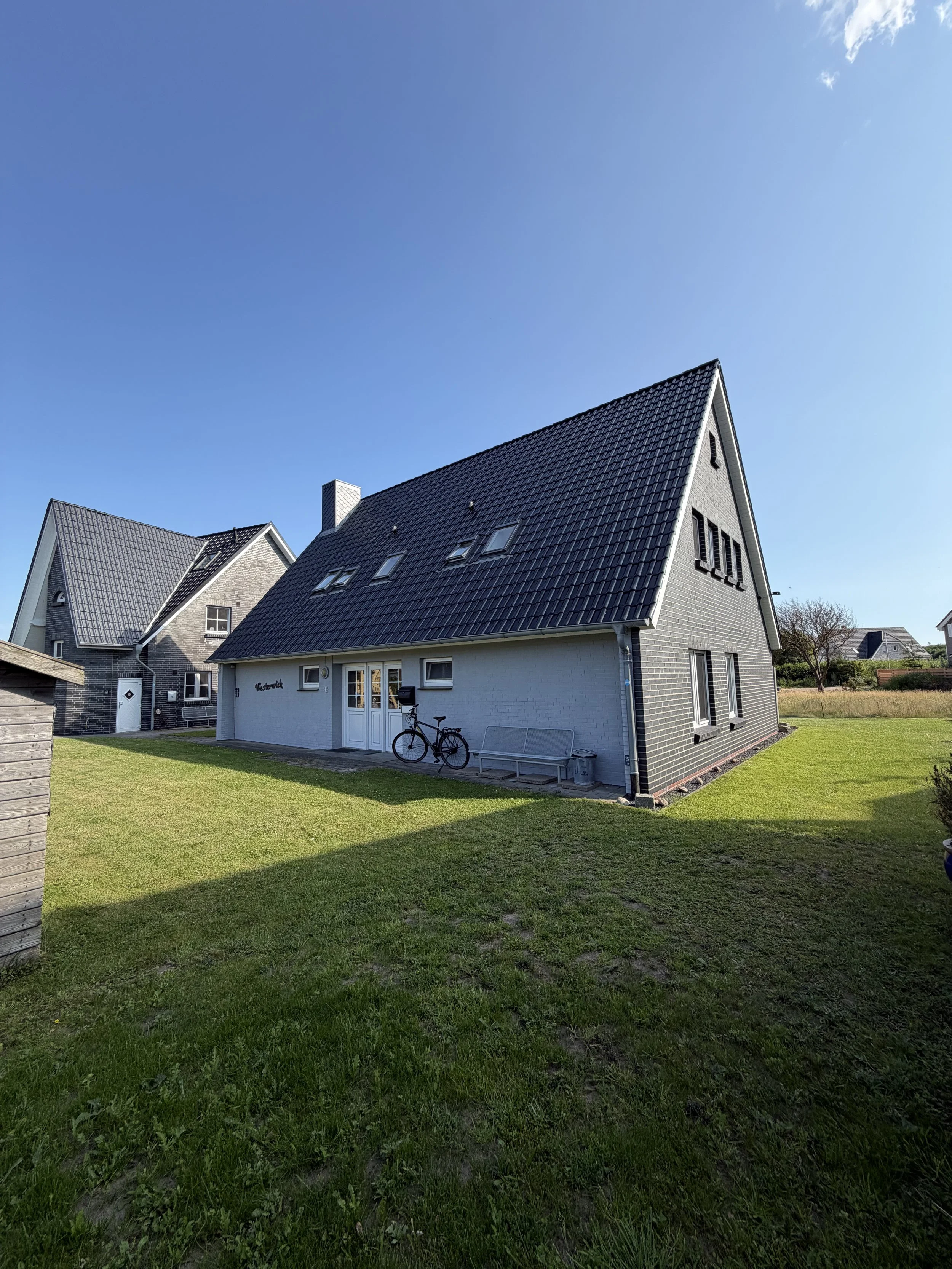 Ein modernes Haus mit dunklem Dach, vor einem grünen Garten und bei sonnigem Himmel