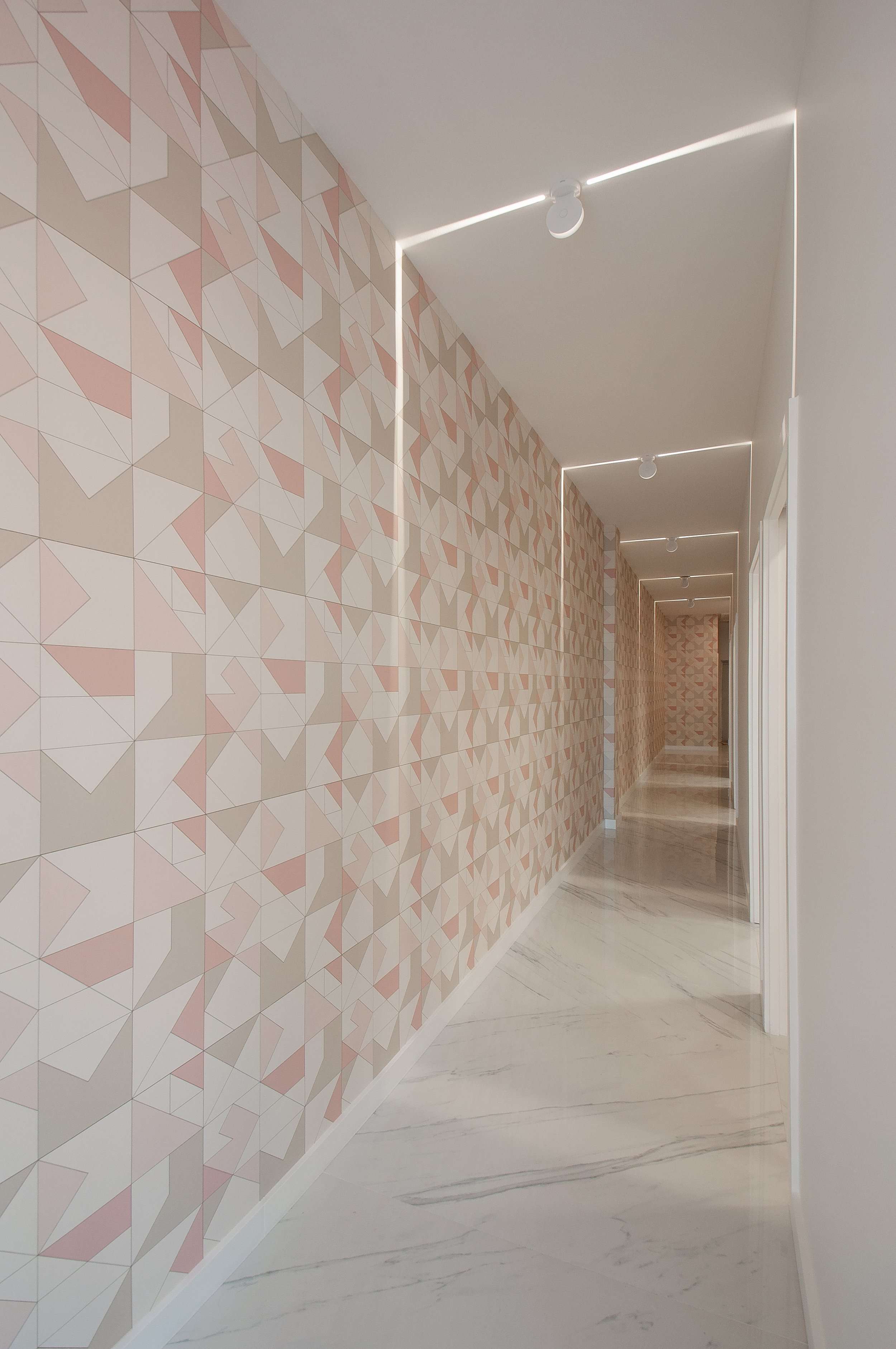 Interior hallway with geometric patterned wall and marble flooring, illuminated ceiling with track lighting.