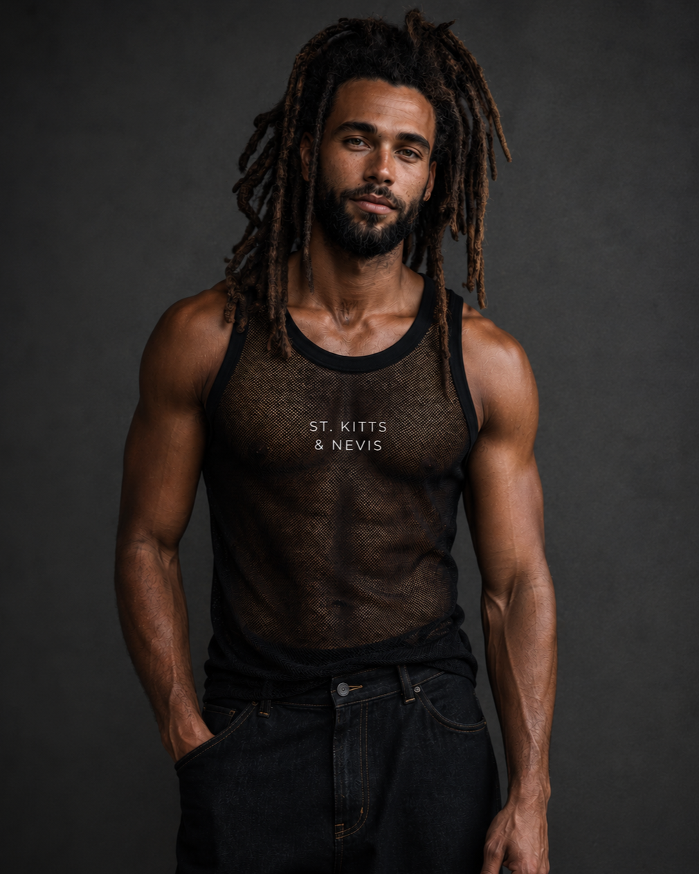 A man with long, dreadlocked hair and a beard wearing a black, sheer tank top with the words 'St. Kitts & Nevis' printed on it, and black jeans, standing against a dark gray background.