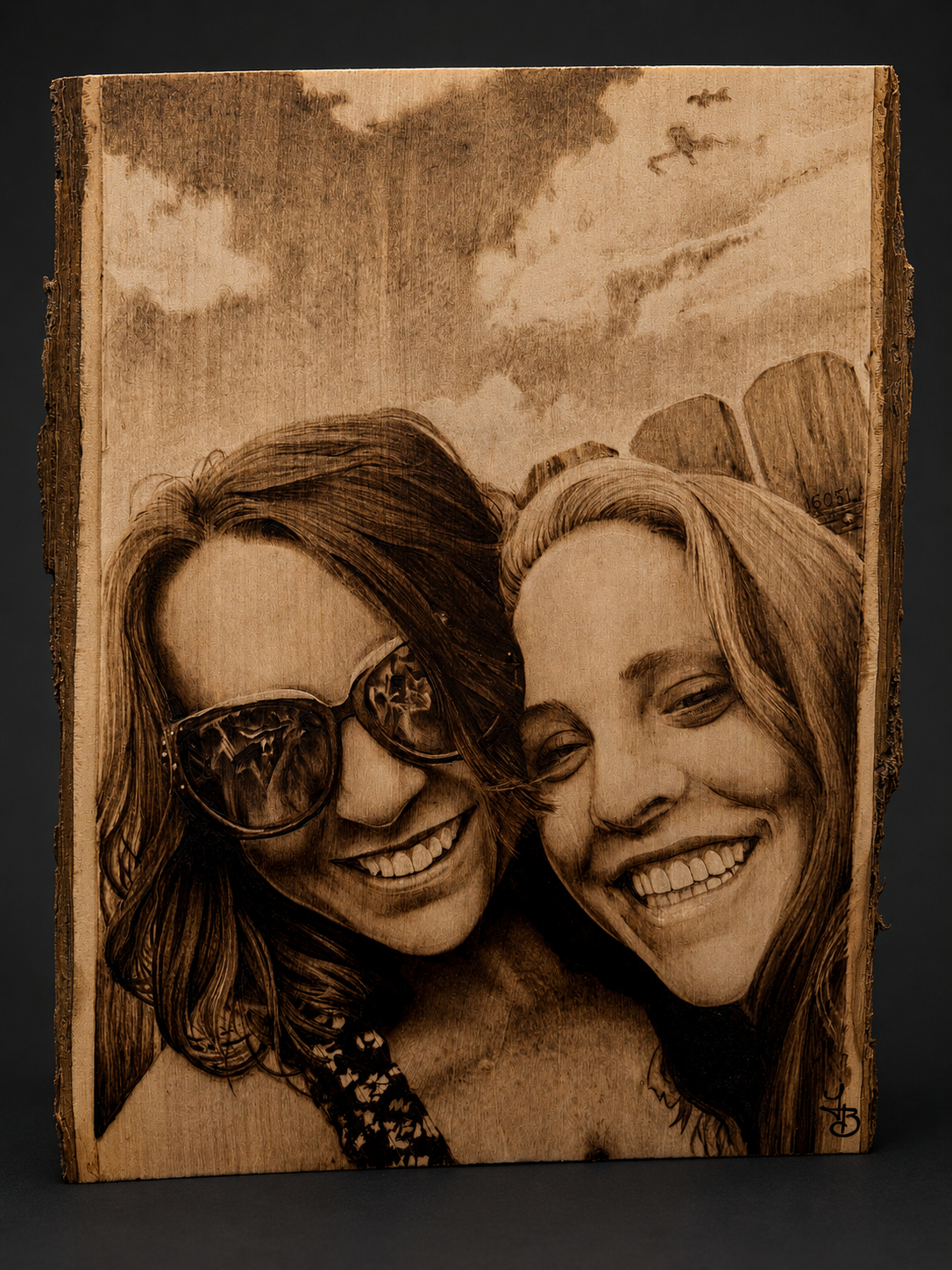 Wooden art piece depicting two smiling women, one wearing sunglasses, with a cloudy sky background.
